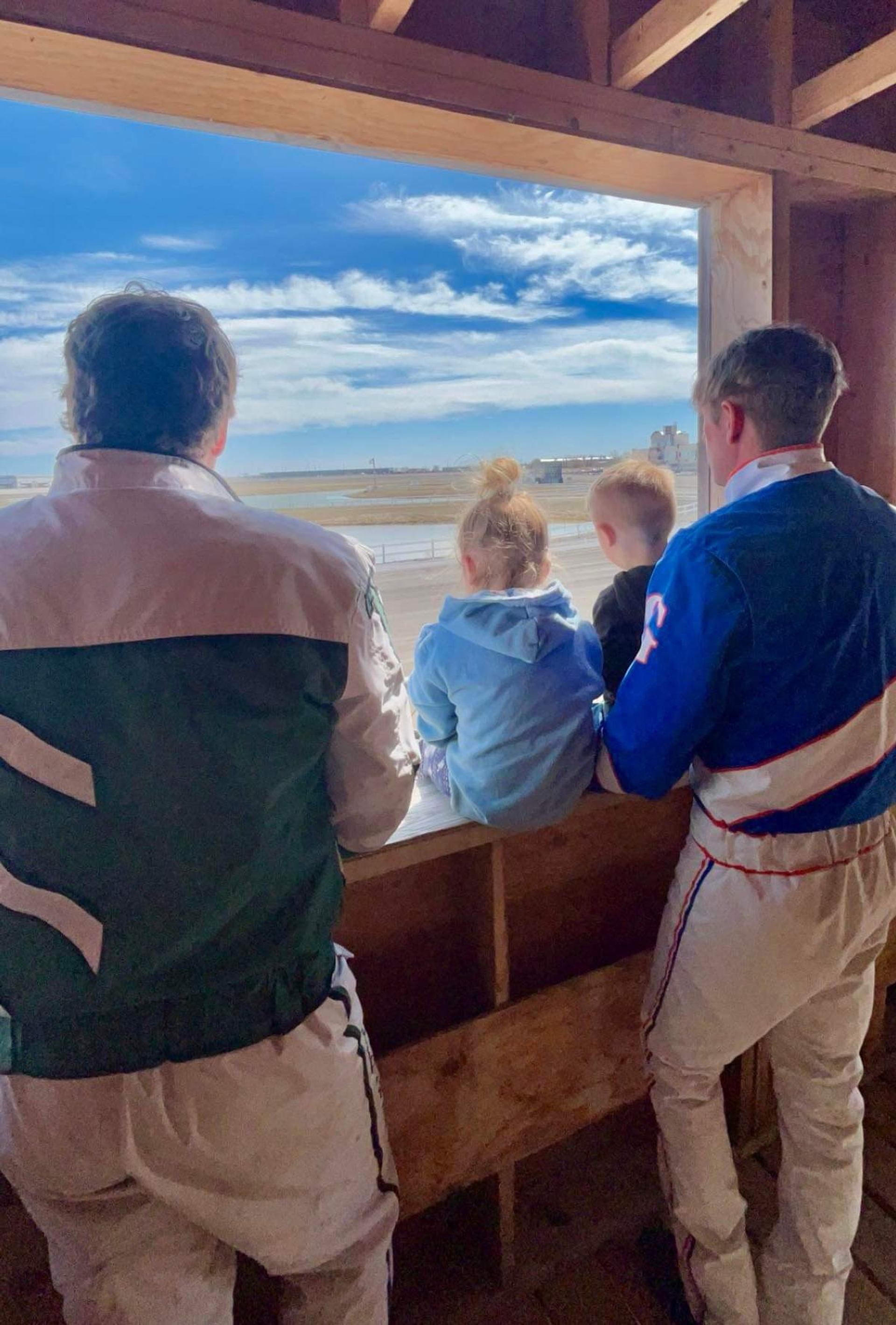 Two race drivers and kids looking out at the track from a wooden paddock