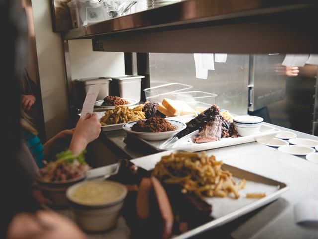 Restaurant kitchen pass with plated meat dishes, fries, and sauces ready to serve.