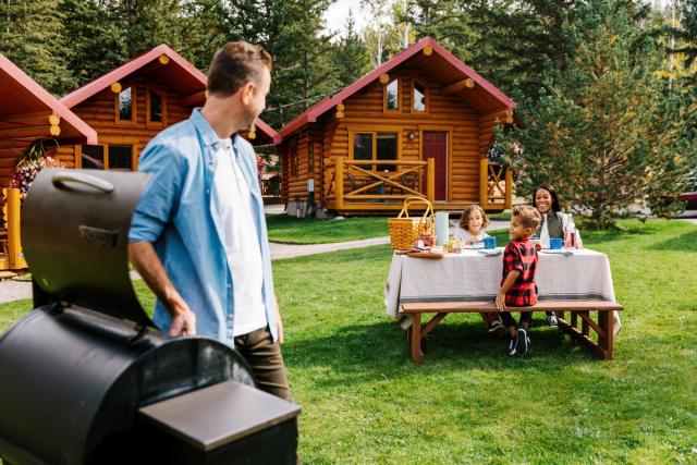 A family BBQ-ing and having a picnic outside of their cabin.