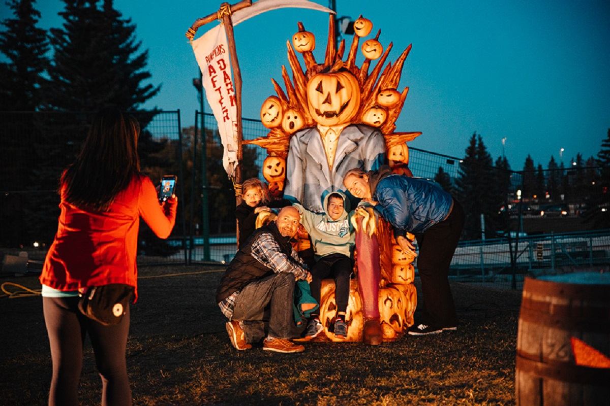 Group posing by pumpkin throne at night in Halloween-themed outdoor display.