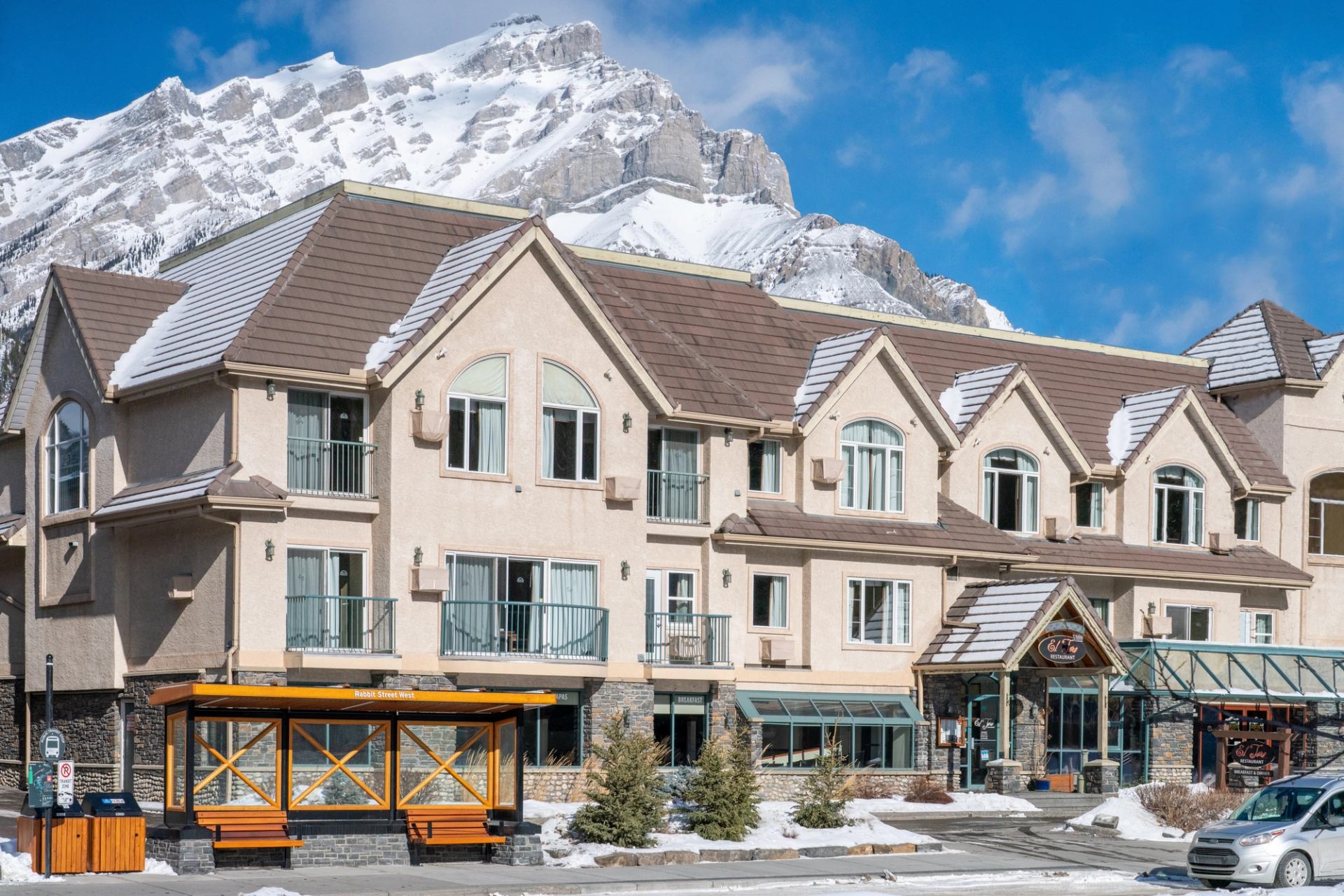 Lodge-style hotel with snowy mountain backdrop and clear blue sky.