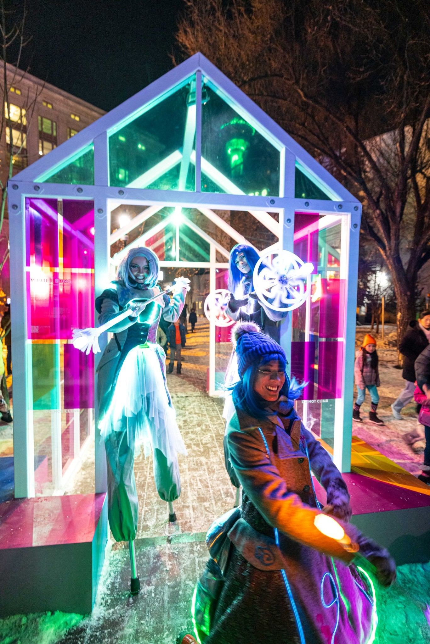 Performers in glowing outfits entertain in lit-up tunnel.