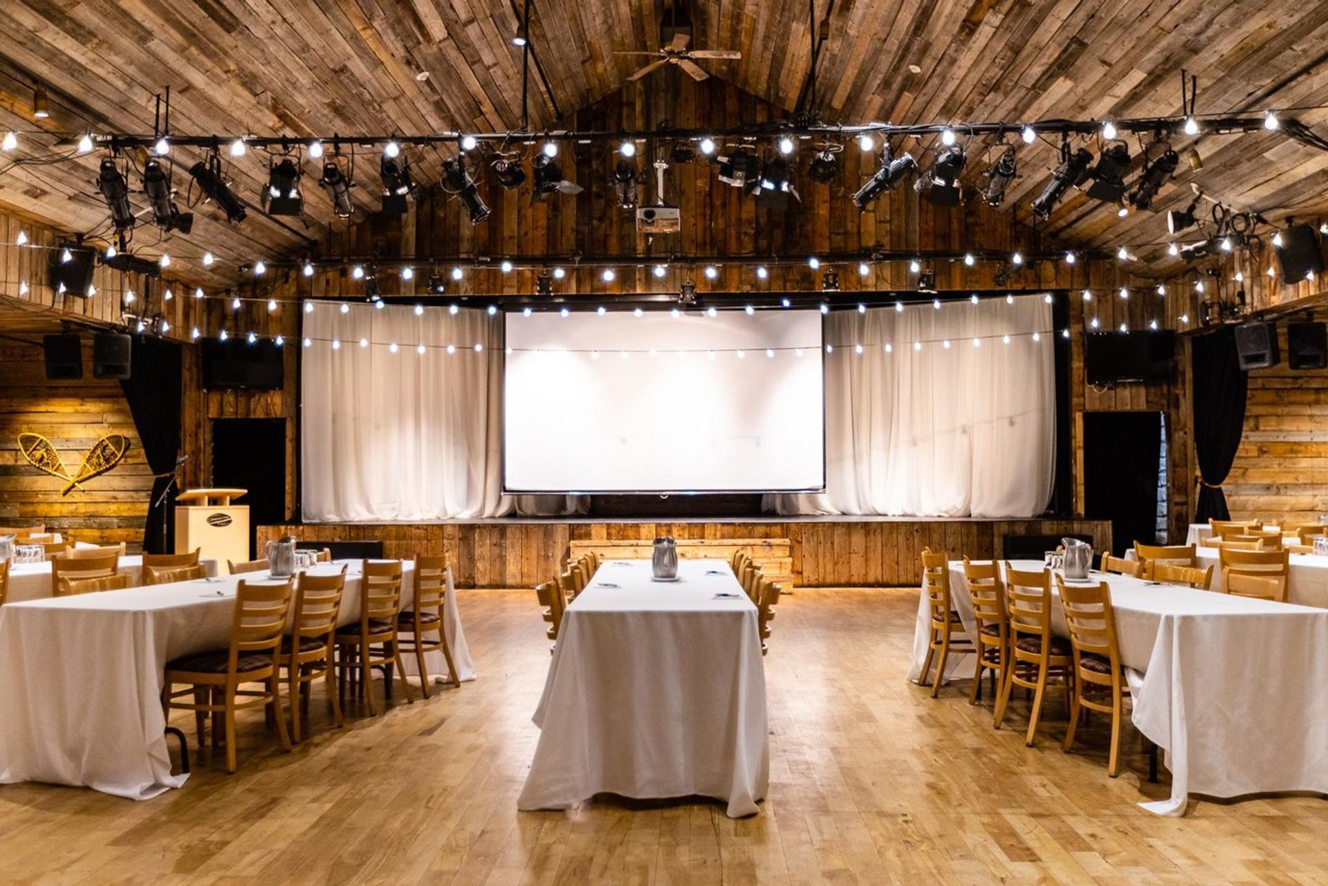 Event setup facing a wooden stage with white curtains and hanging string lights.