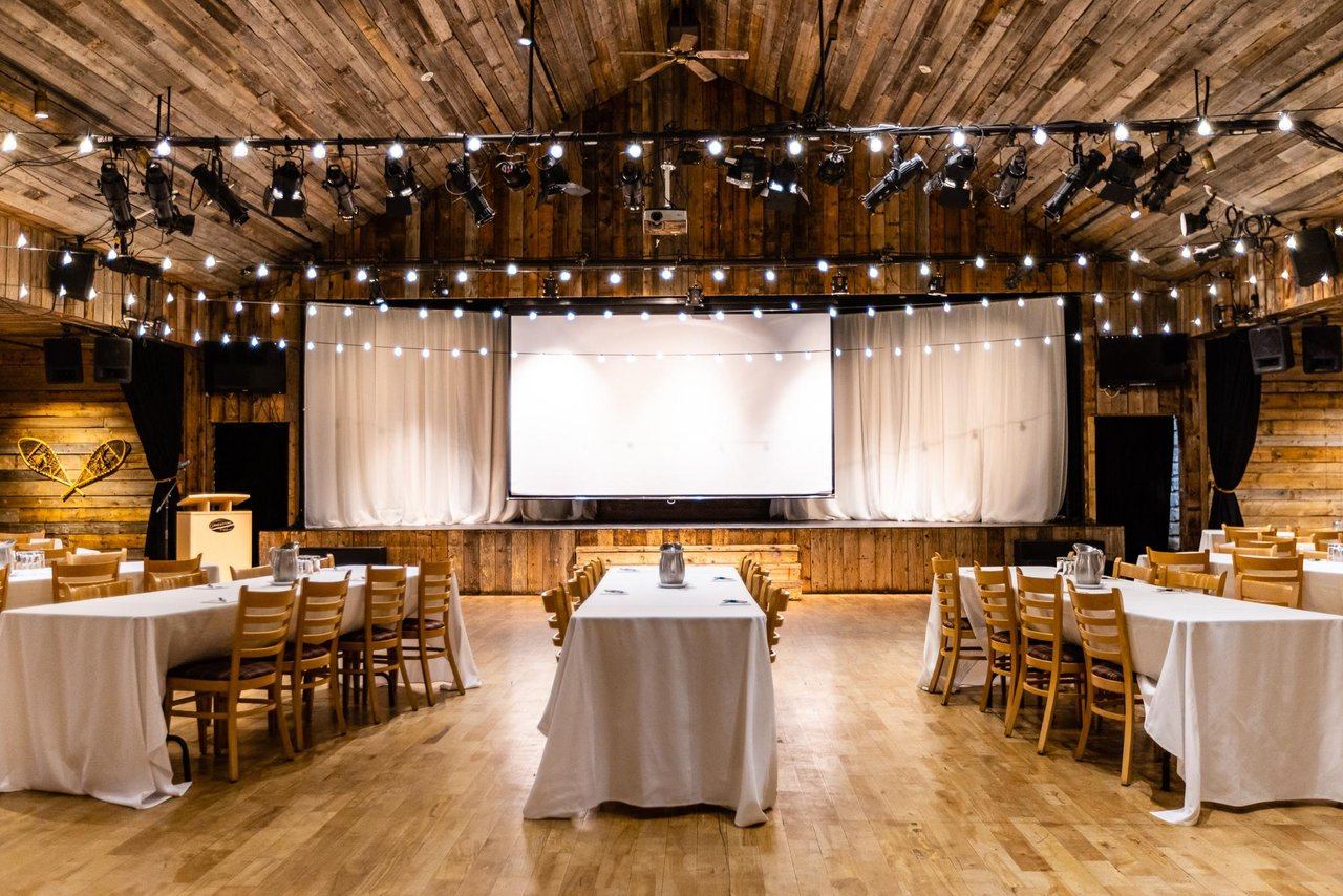 Event setup facing a wooden stage with white curtains and hanging string lights.