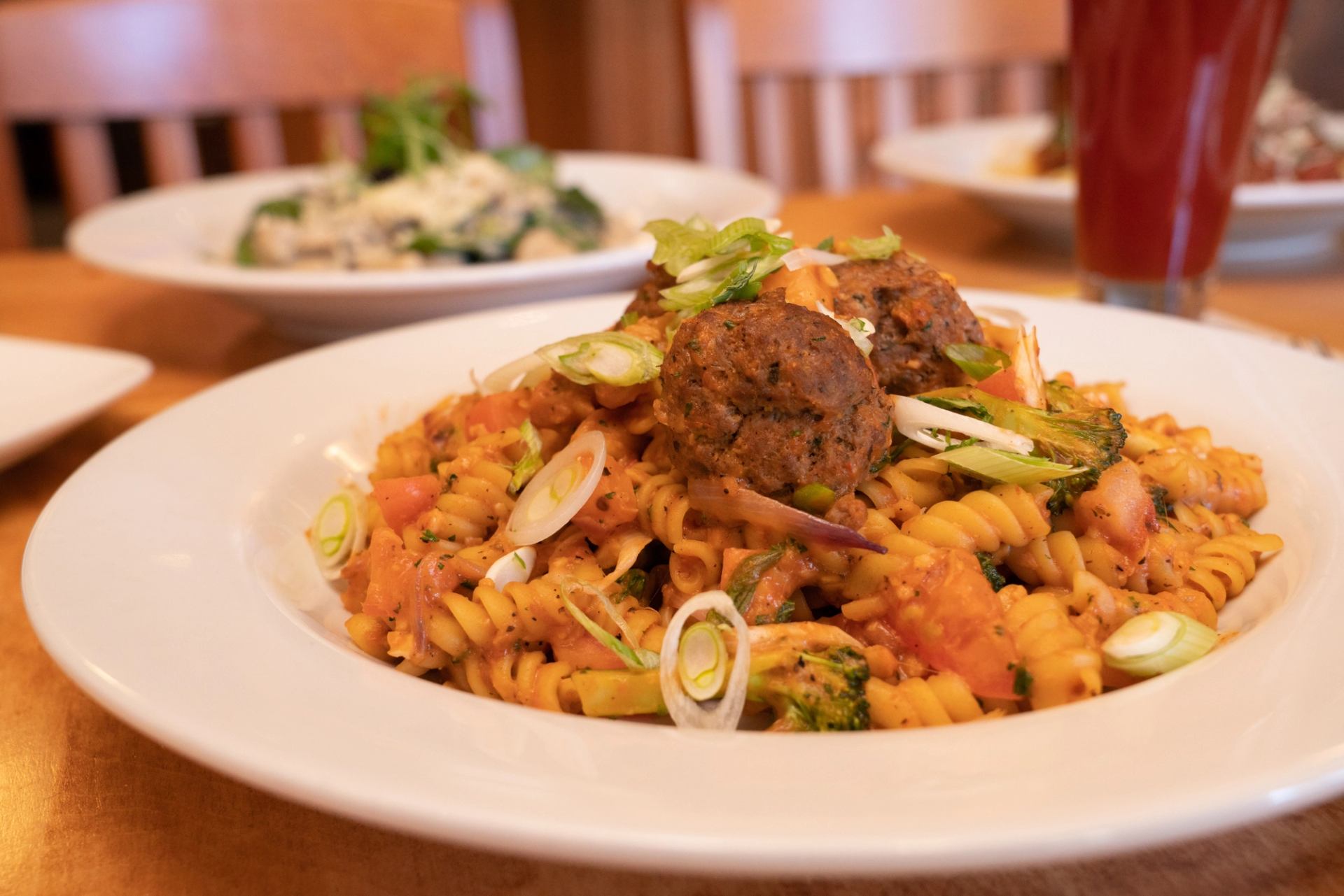 Fusilli pasta with tomato sauce, meatballs, veggies, and green onion garnish.
