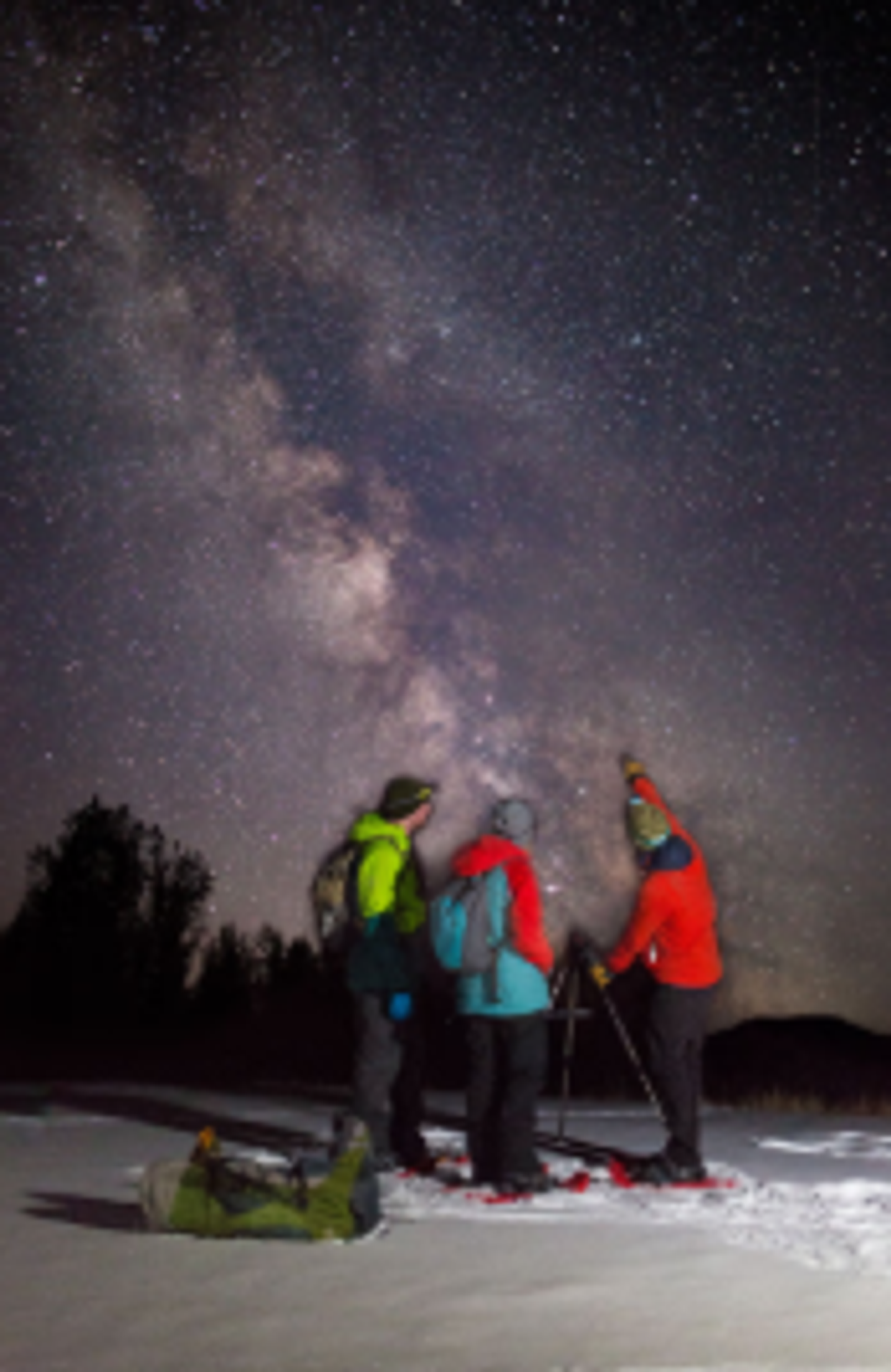 Three snowshoers look up at the brilliant Milky Way at night.