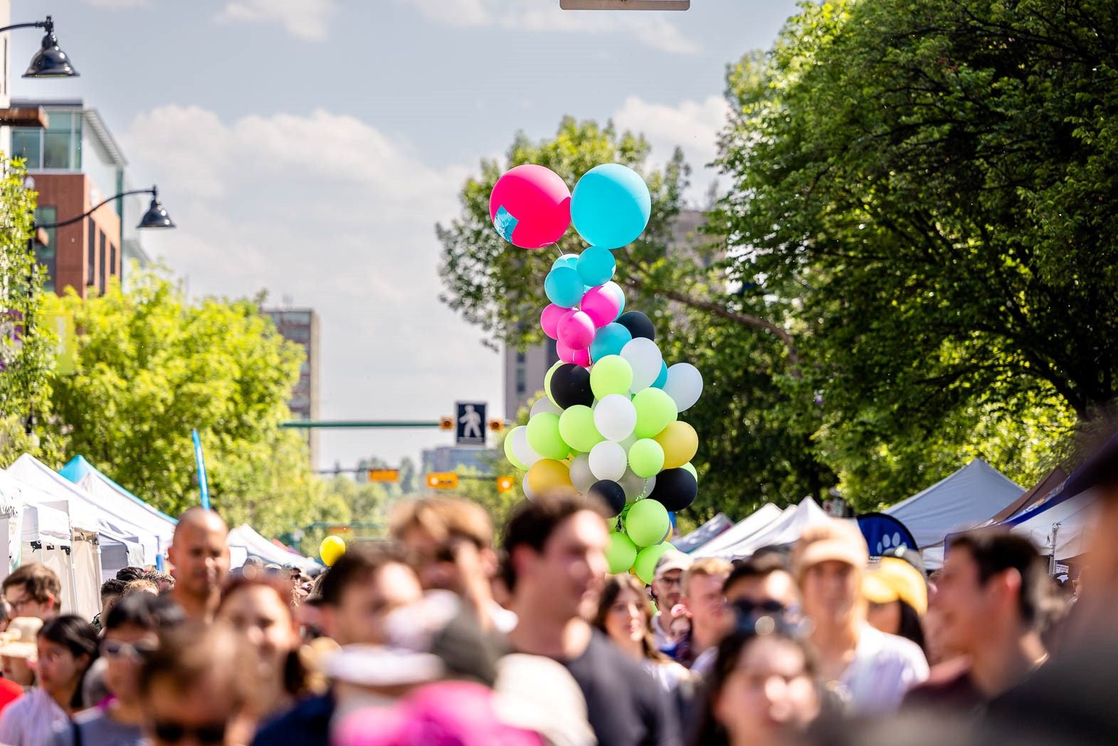 Colorful balloon display rising above a crowded street lined with festival tents.