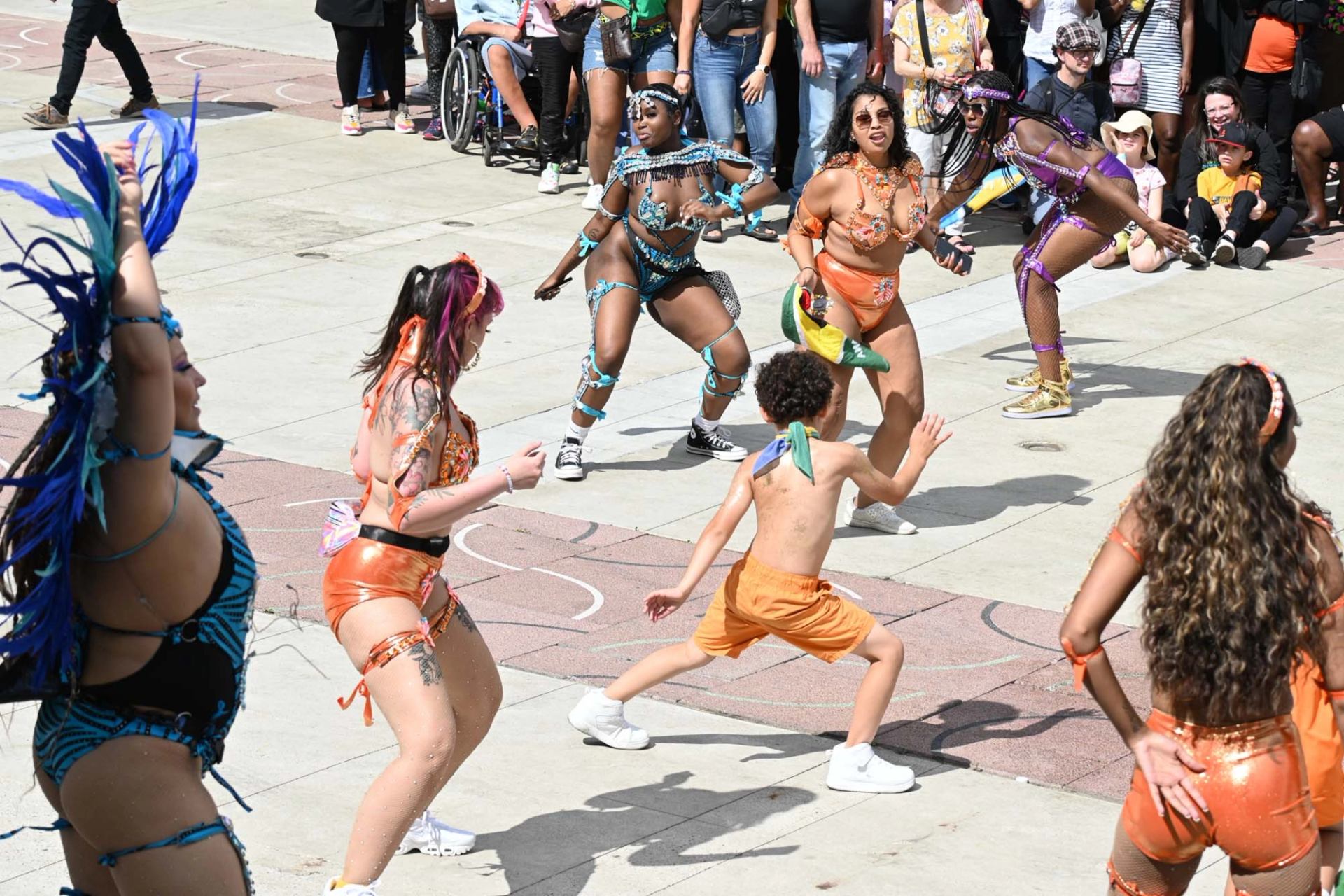Street performers in colourful carnival costumes dance in a circle before a crowd..