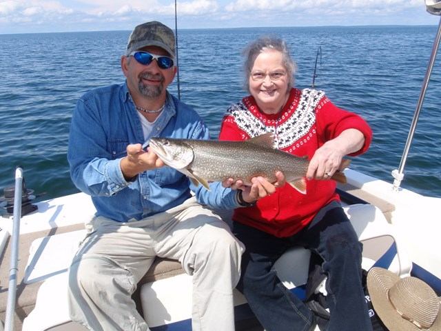 Two people on a boat showing off a big fish they caught on a sunny day.