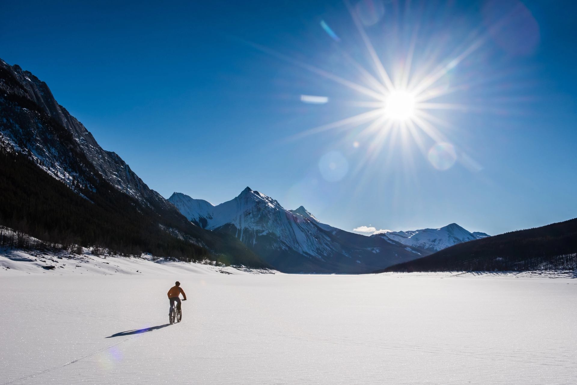 A man fat biking on Maligne Lake on sunny winter day in Jasper National Park.