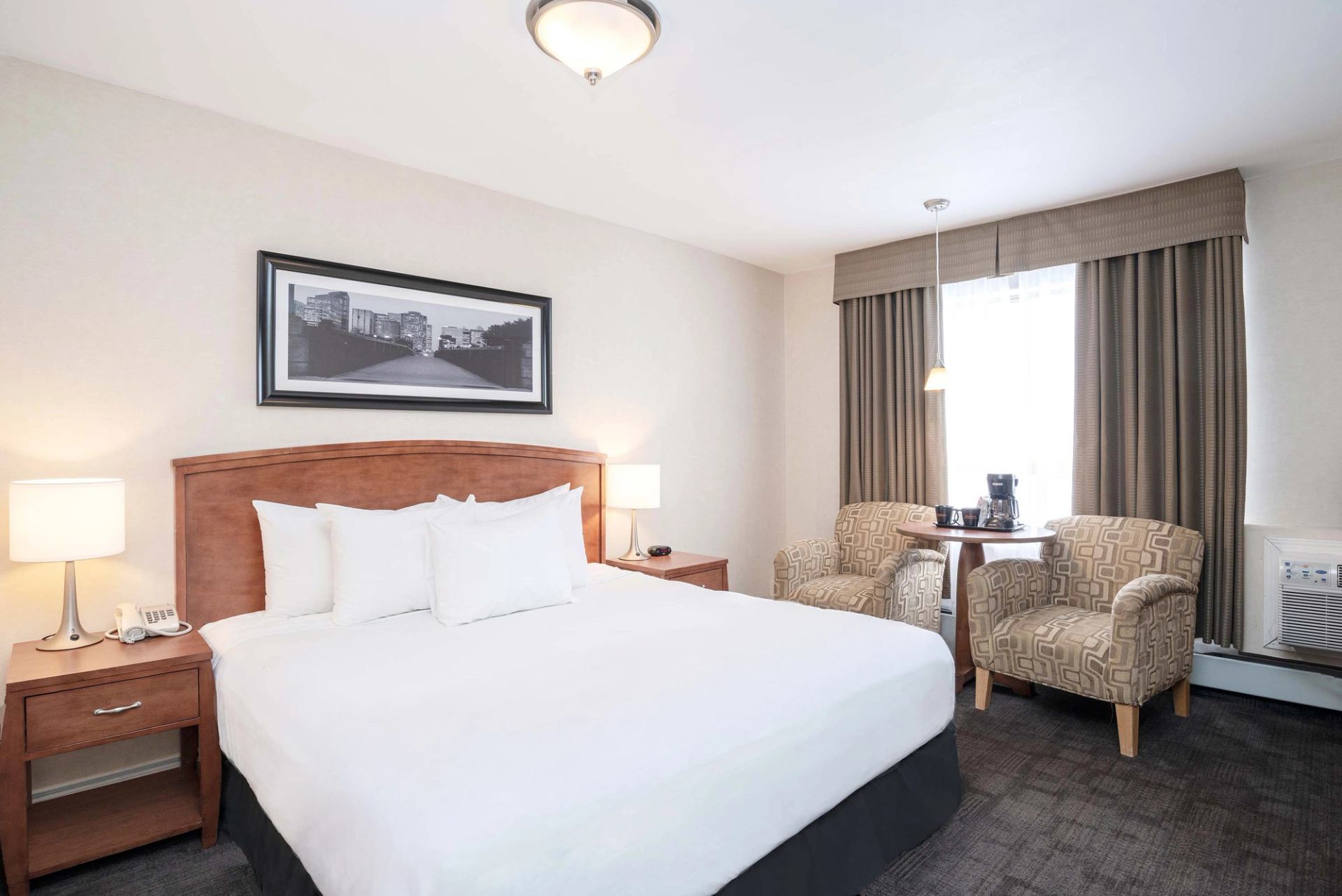 Hotel room with king bed, nightstands, two armchairs, small table and window.