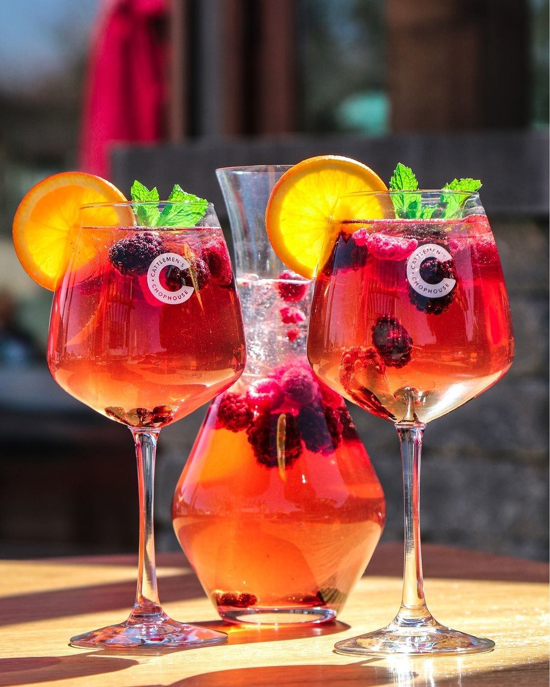 Red drinks with fruit garnish and googly eyes in glasses, served outdoors on a sunny day.