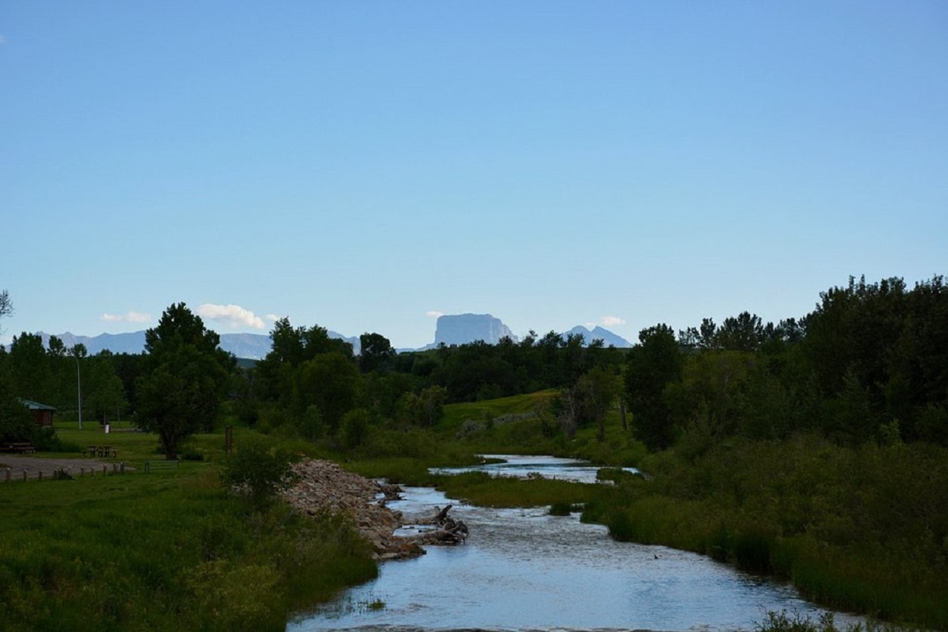 River winding through green trees and grass with distant flat-topped mountain under clear sky.