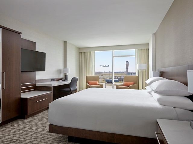 Hotel room with airport runway view, modern furniture, and large bed.