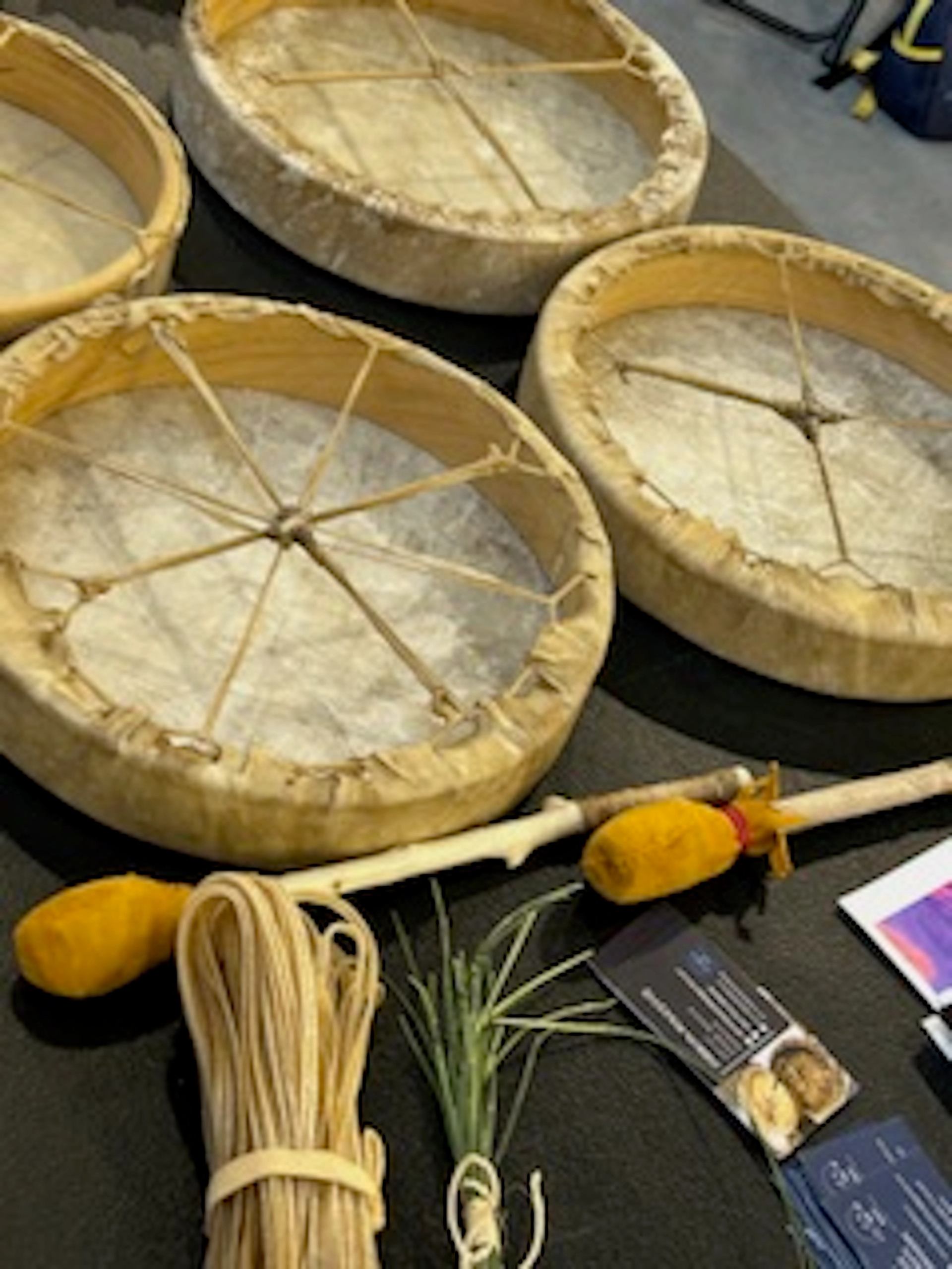 Hand drums, drumsticks, plant fibres and printed cards arranged on a dark table.