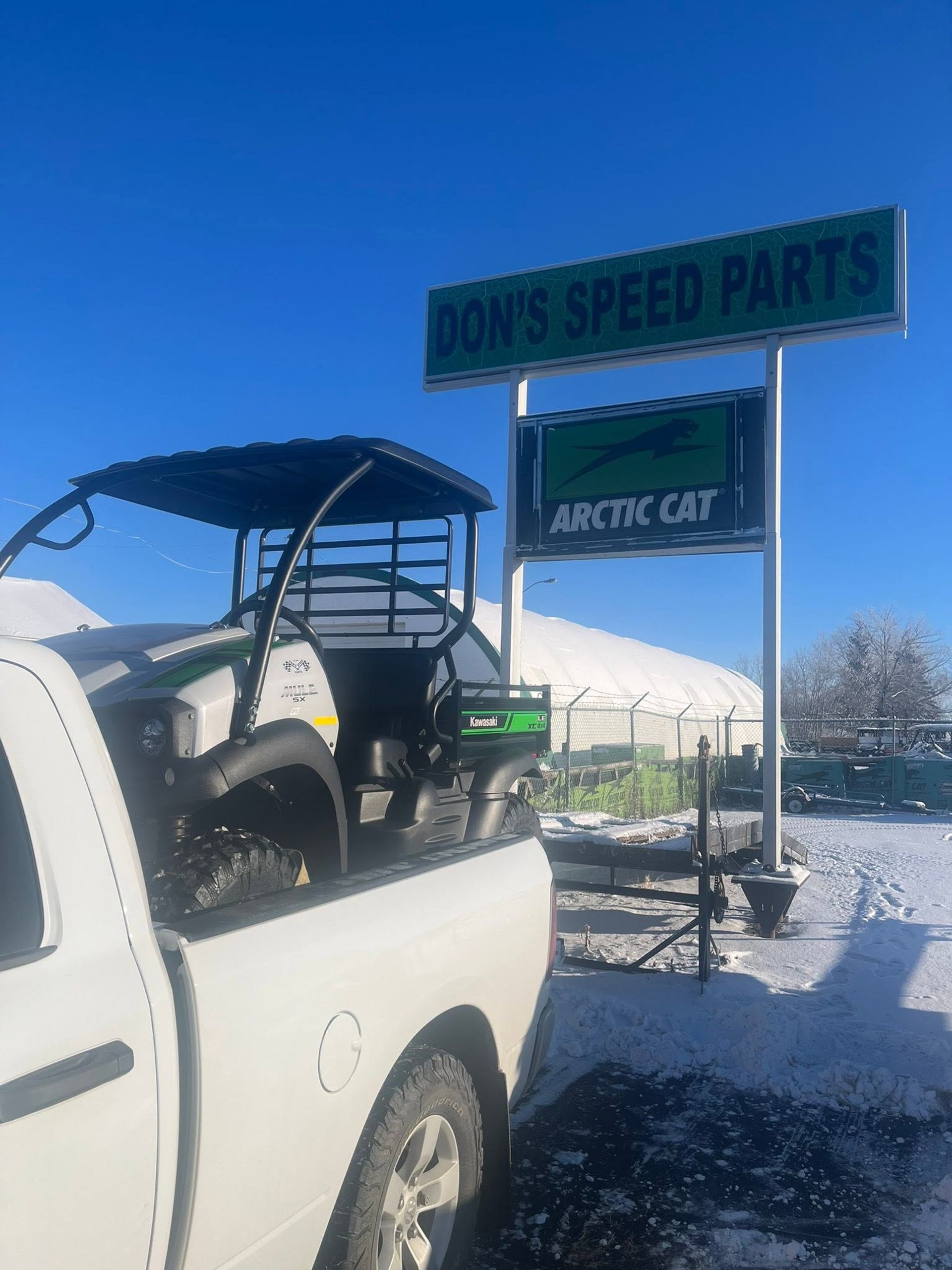 Utility vehicle in pickup truck beneath Don's Speed Parts and Arctic Cat signs.