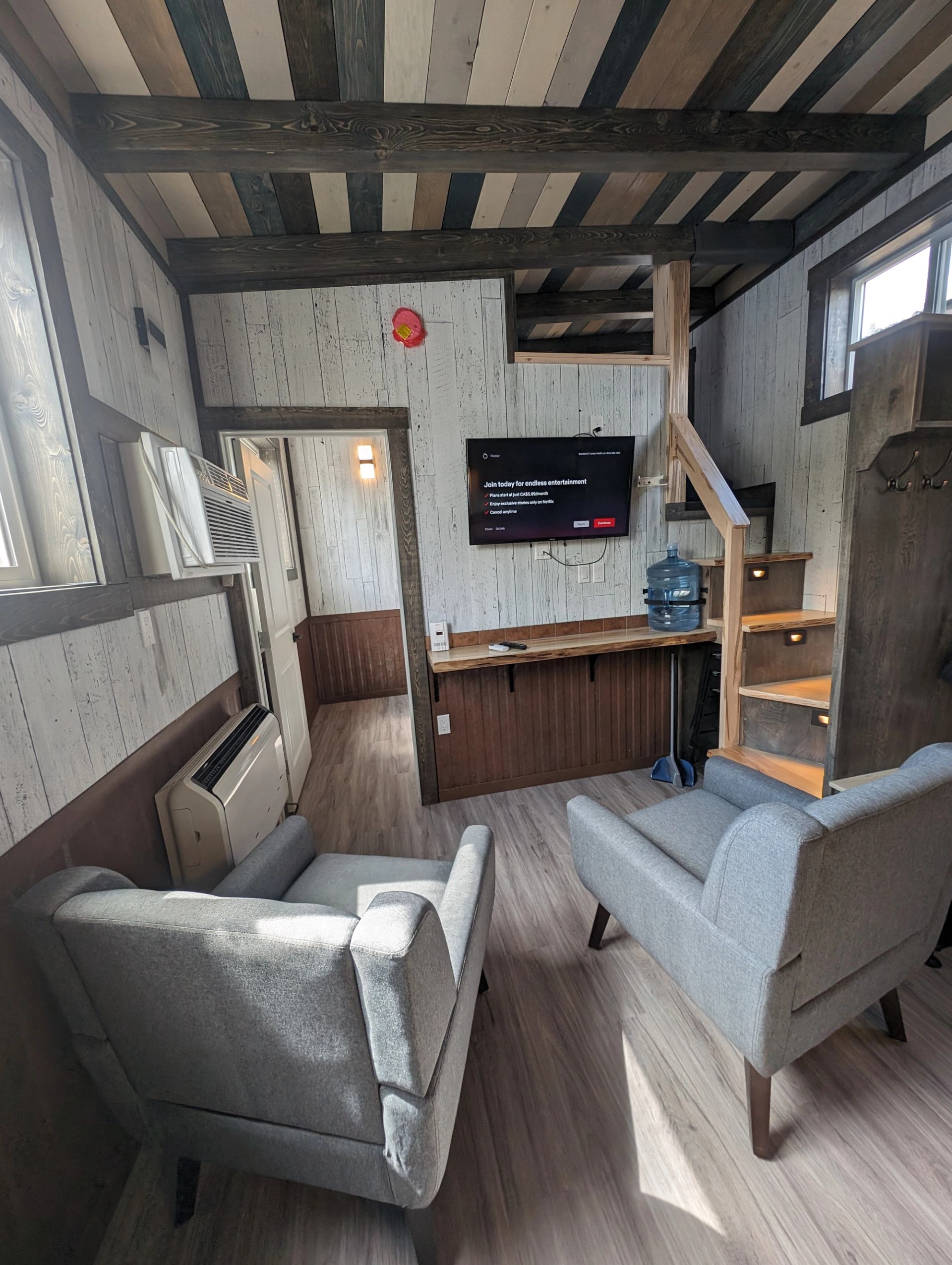 Compact wood-panelled room with armchairs, wall-mounted TV and stairs to a loft.