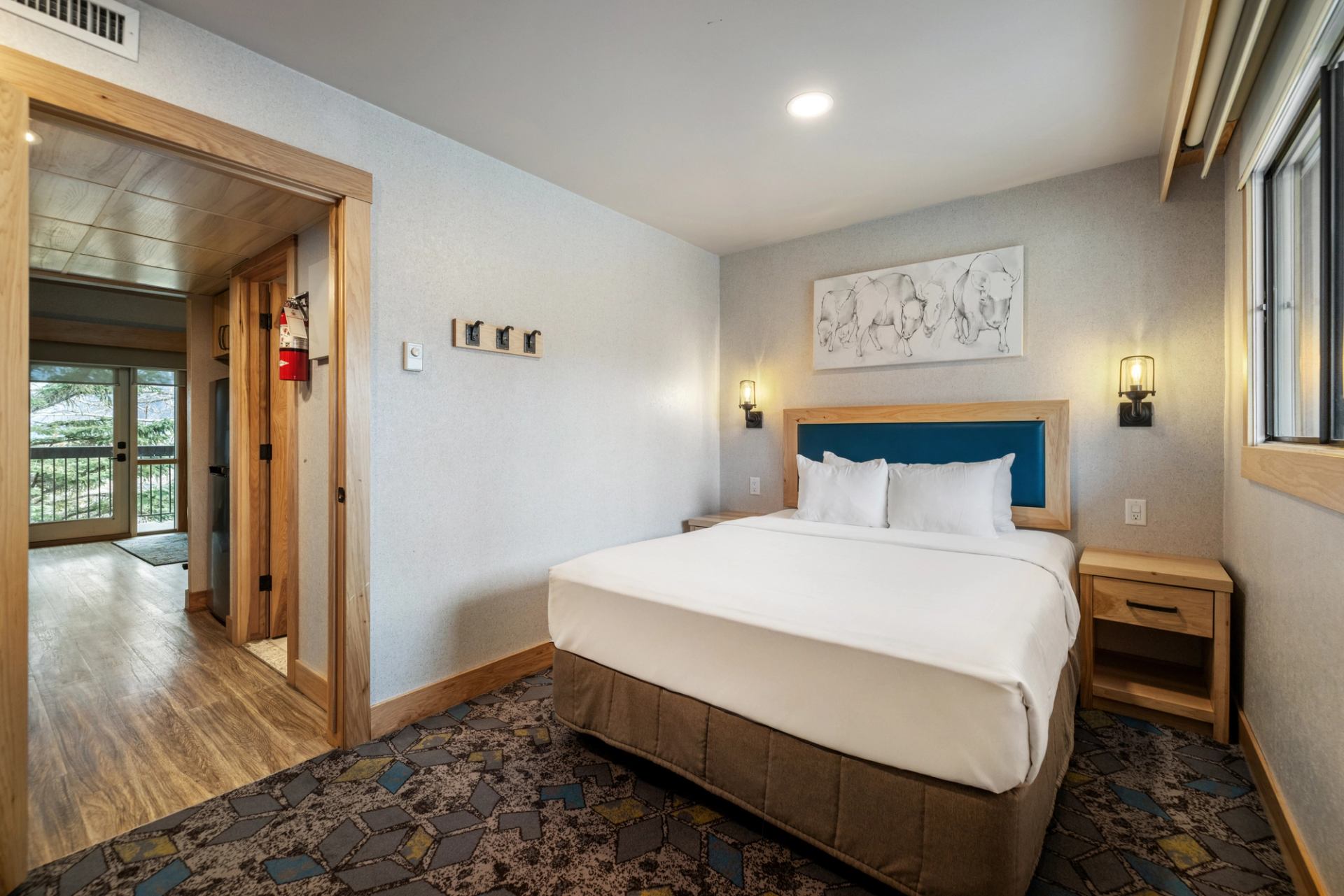 Cozy bedroom with teal headboard, white linens, and view of the hallway through the open door.