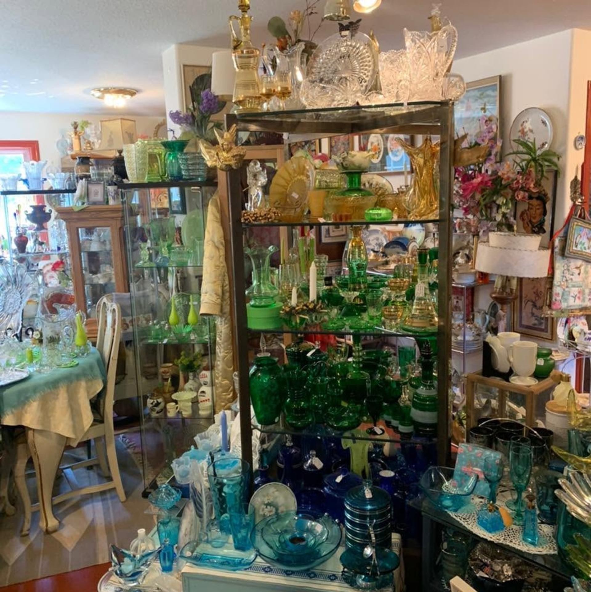 Crowded antique shop interior with shelves of colourful glassware, dishes and decorative items.