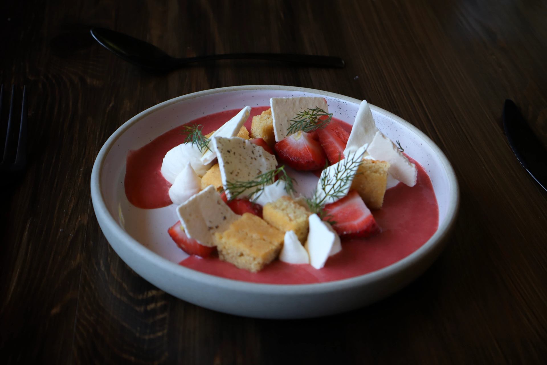 Dessert plate with strawberries, meringue, sponge cubes, and pink sauce on a white dish.
