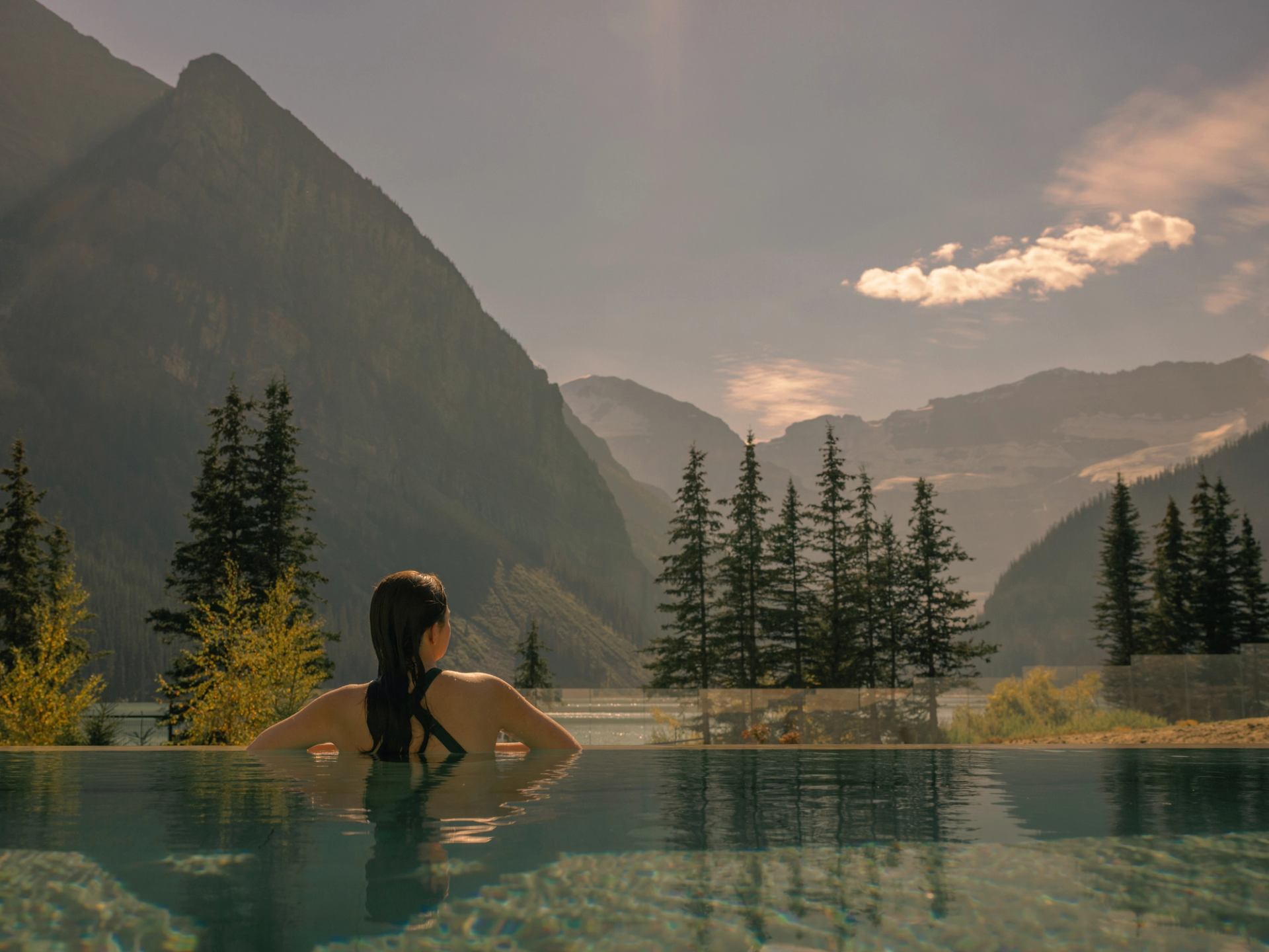 A woman in a bathing suit stands in a pool while admiring the Canadian Rockies.