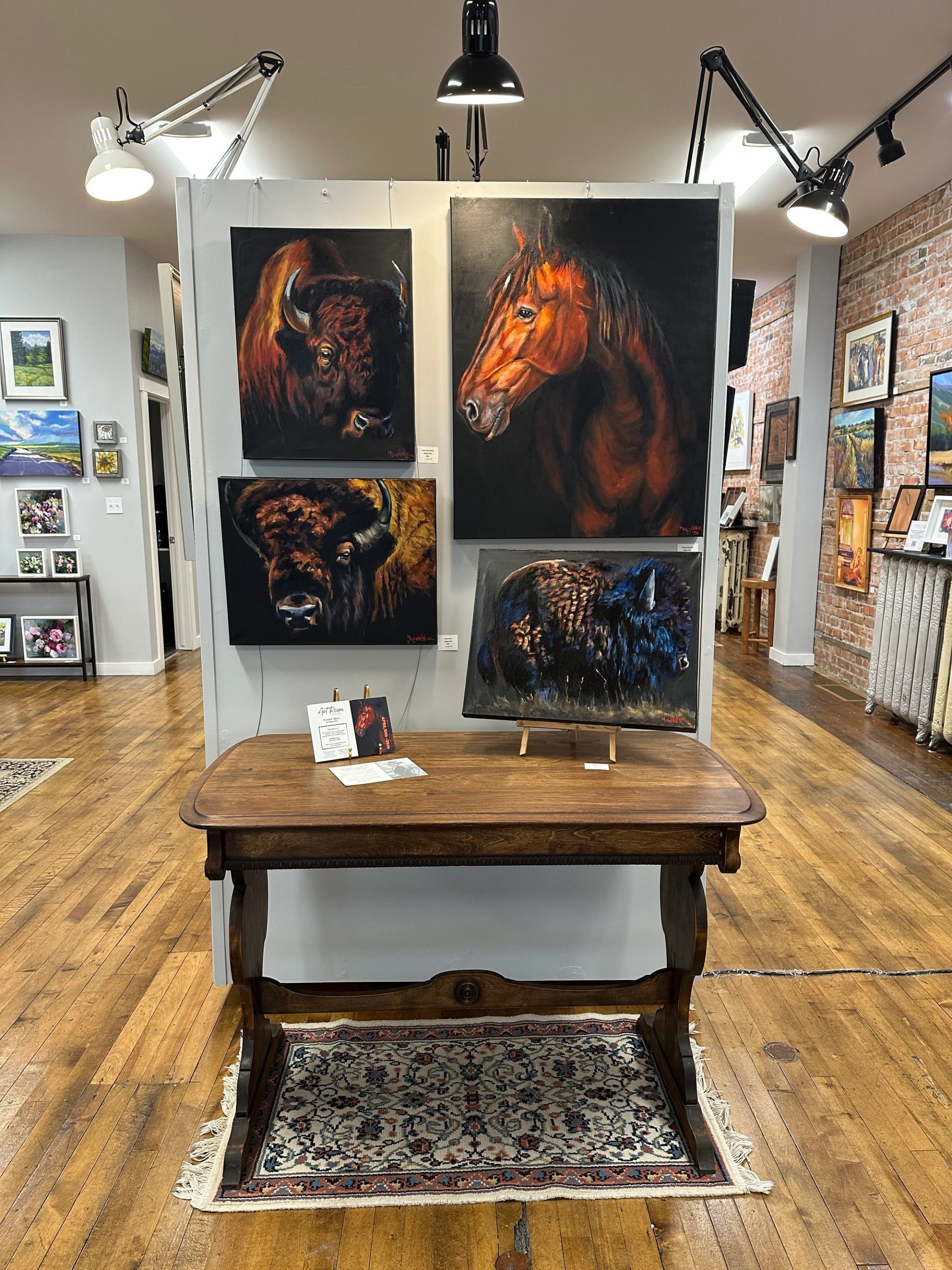 Paintings of bison and a horse displayed on a freestanding gallery wall.