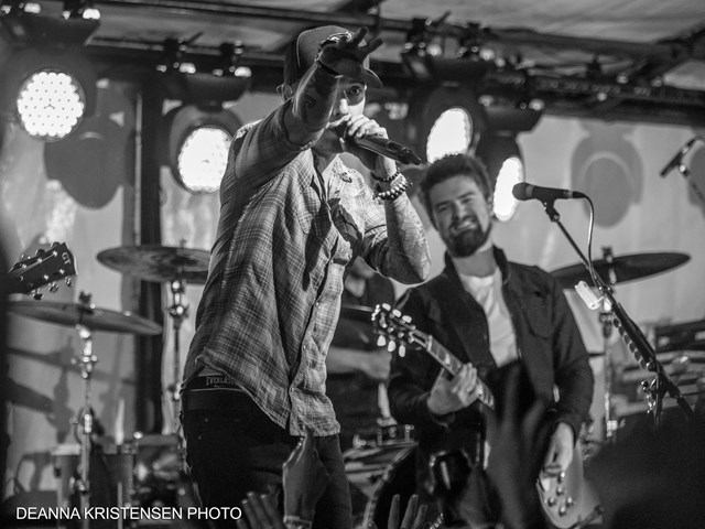 Black and white photo of band performing on stage with bright lights and instruments.