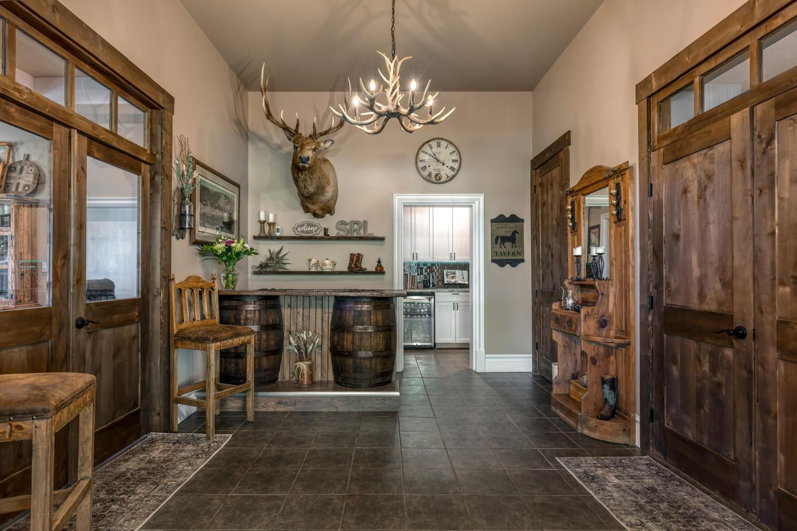 Rustic entryway with mounted deer head, antler chandelier and barrel bar.