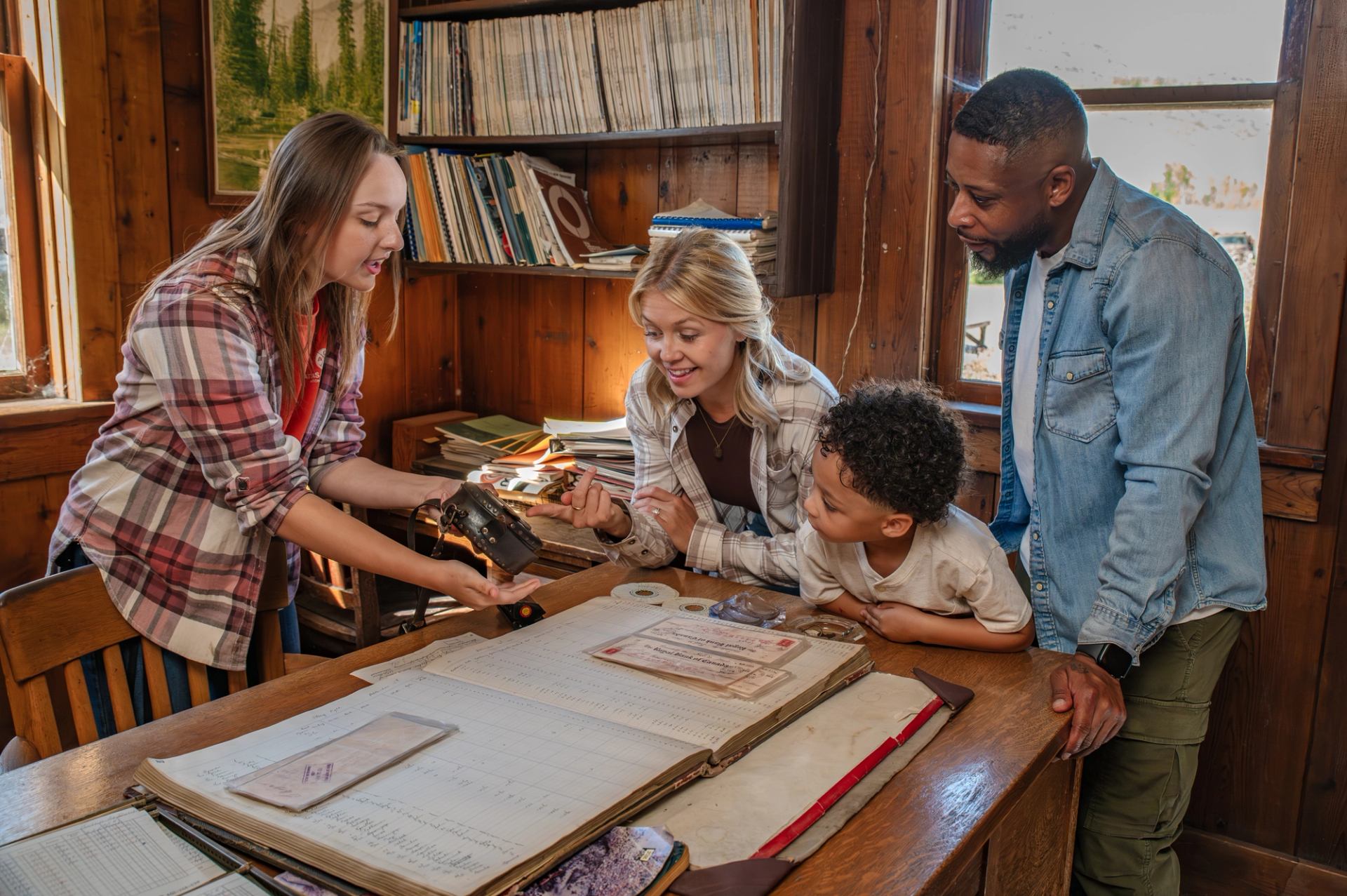 Museum staff member shows an old camera to visitors at a wooden desk with records.