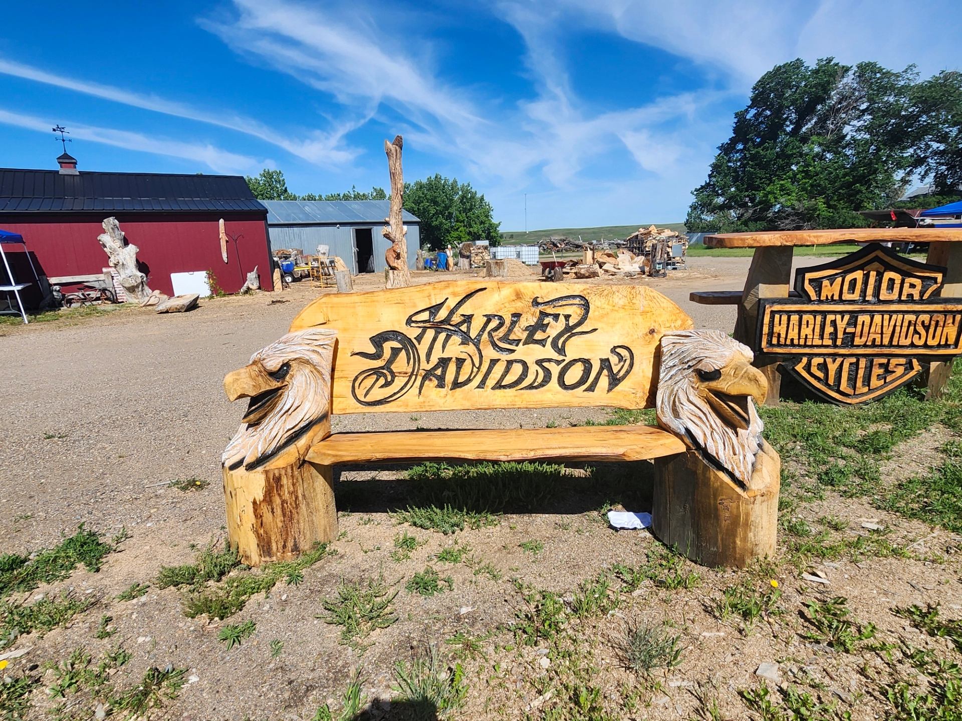 Wooden Harley-Davidson bench with carved eagle heads in outdoor workshop yard.