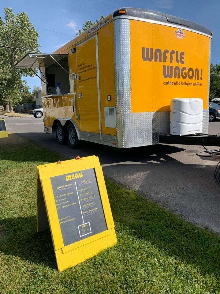 Bright yellow Waffle Wagon food trailer with menu board on grass