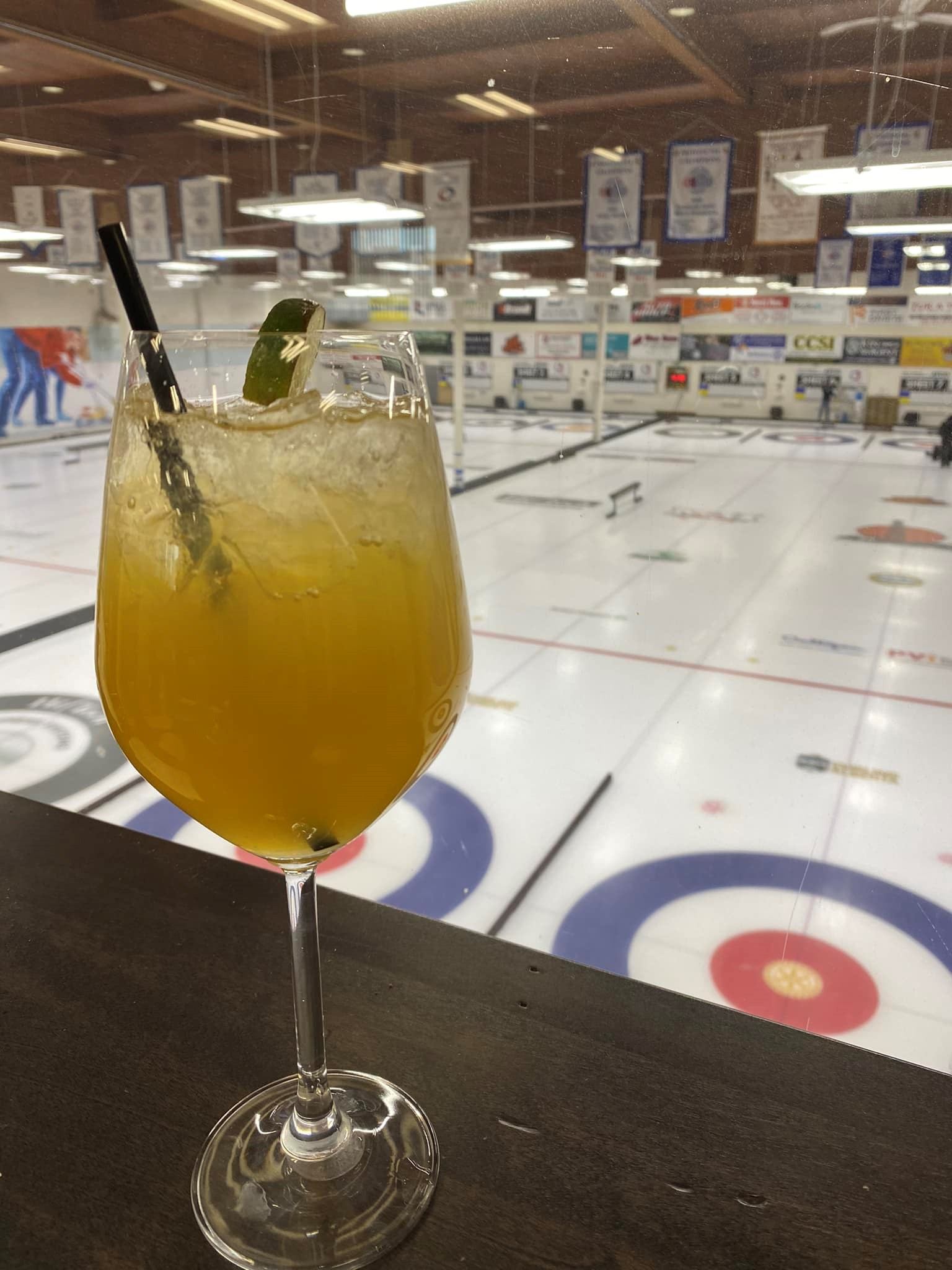 Cocktail glass with lime wedge and straw overlooking indoor curling rink.