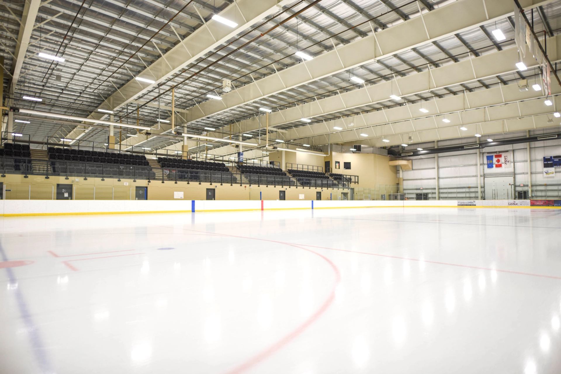 Indoor ice rink with marked lines, boards, and empty spectator seating.