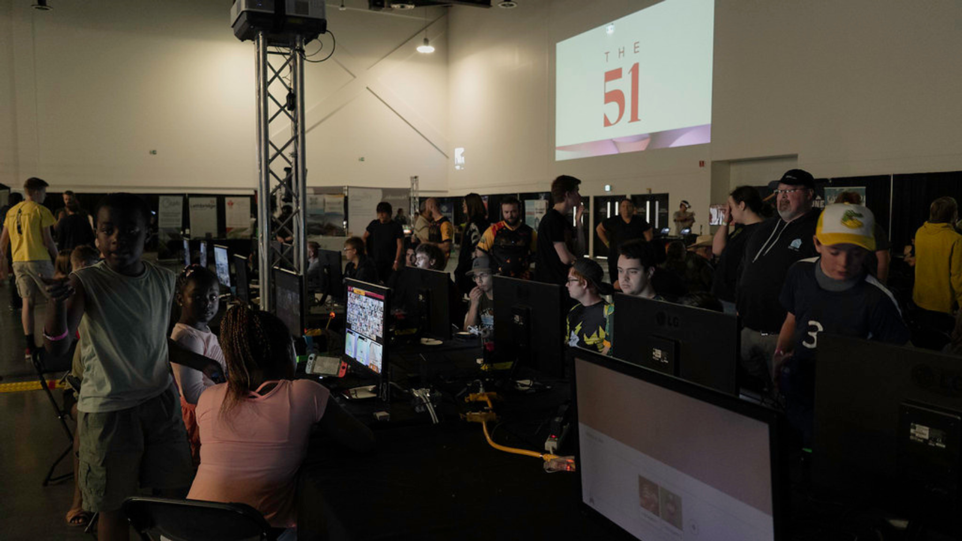 Crowded event space with people using computers and gaming stations during a tech conference.