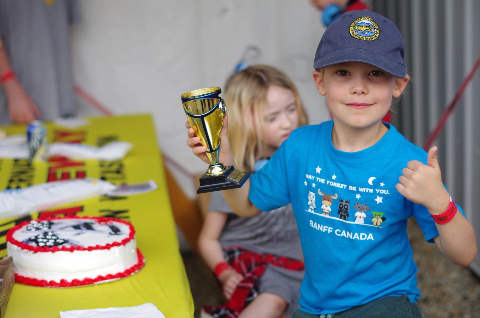 Child holding a trophy beside a racing-themed cake on a table at the track.