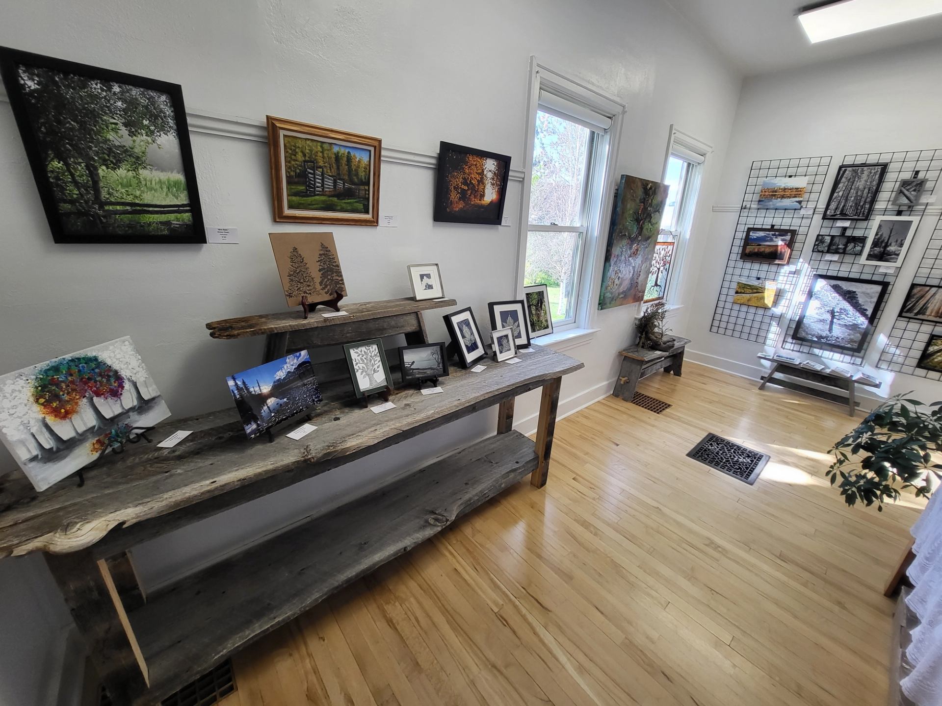 Exhibit room with framed paintings, small artworks, and display tables near windows.