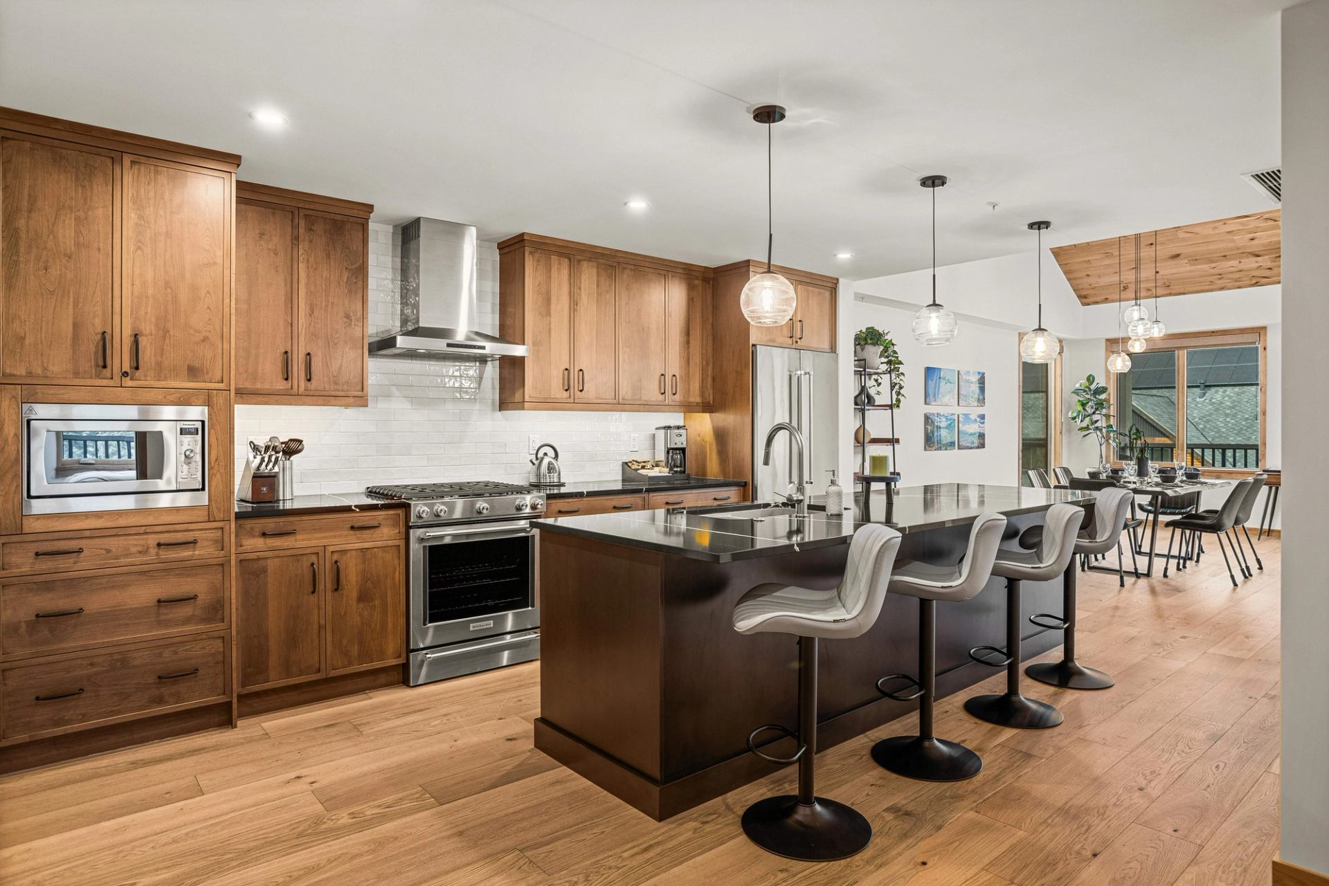 Open kitchen and dining area with wood cabinetry, island seating and pendant lights.
