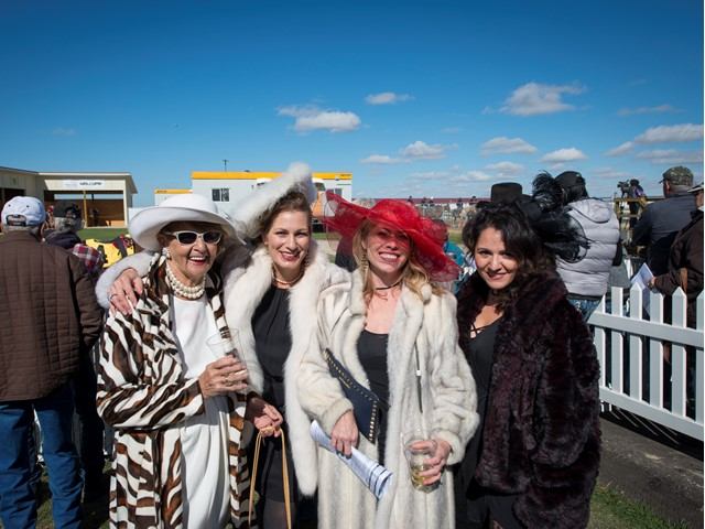 Elaborately dressed women pose for a race day photo.