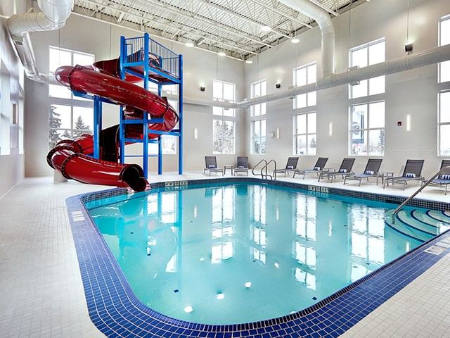 Indoor pool with red slide, lounge chairs, and natural light.