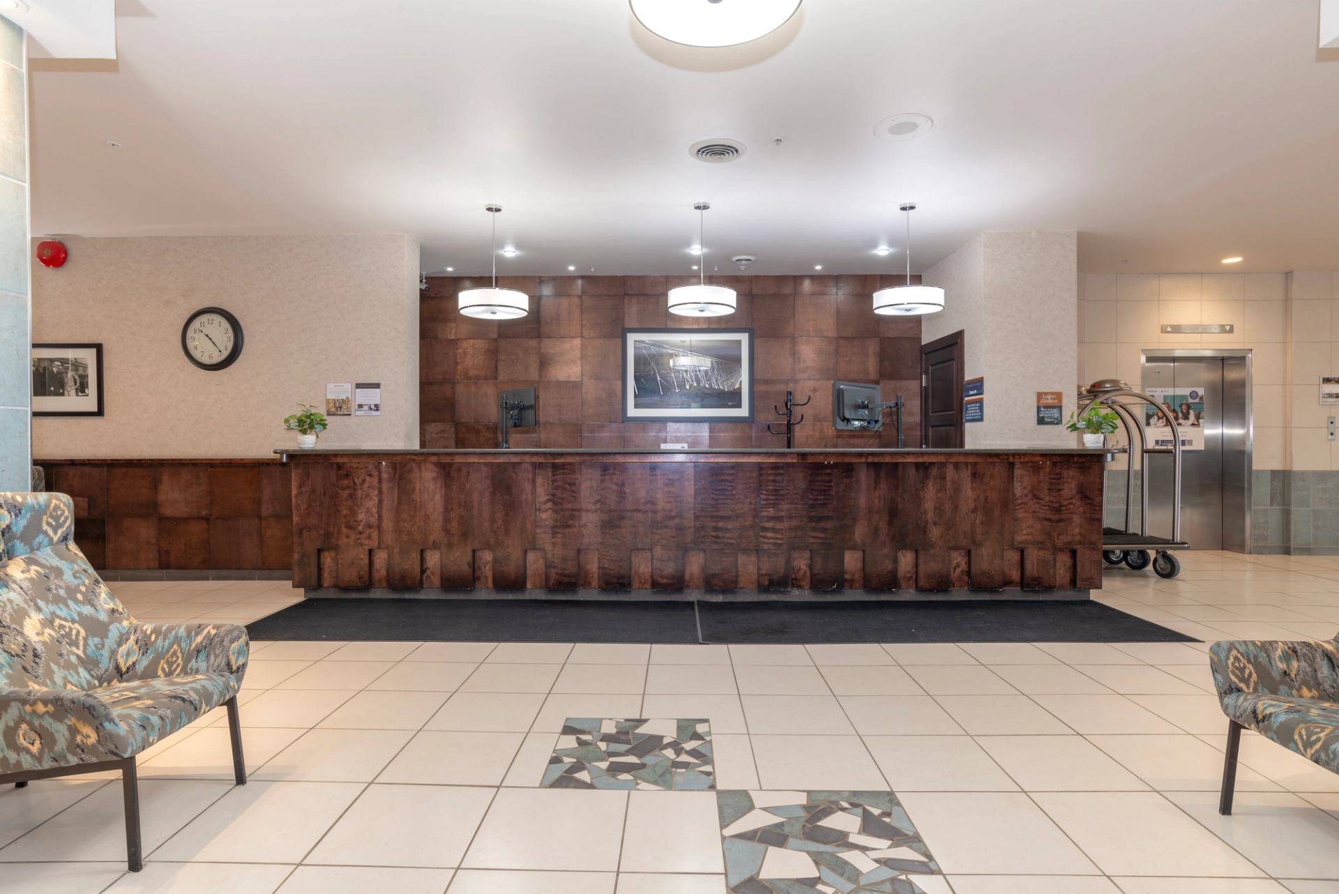 Open hotel lobby with long front desk, seating area, and elevator access.