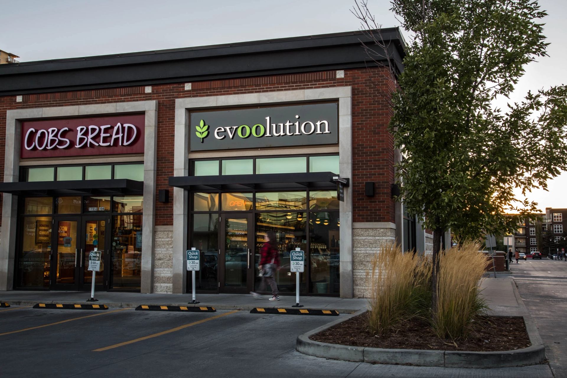 Evoolution storefront beside COBS Bread, with parking and greenery at sunset.