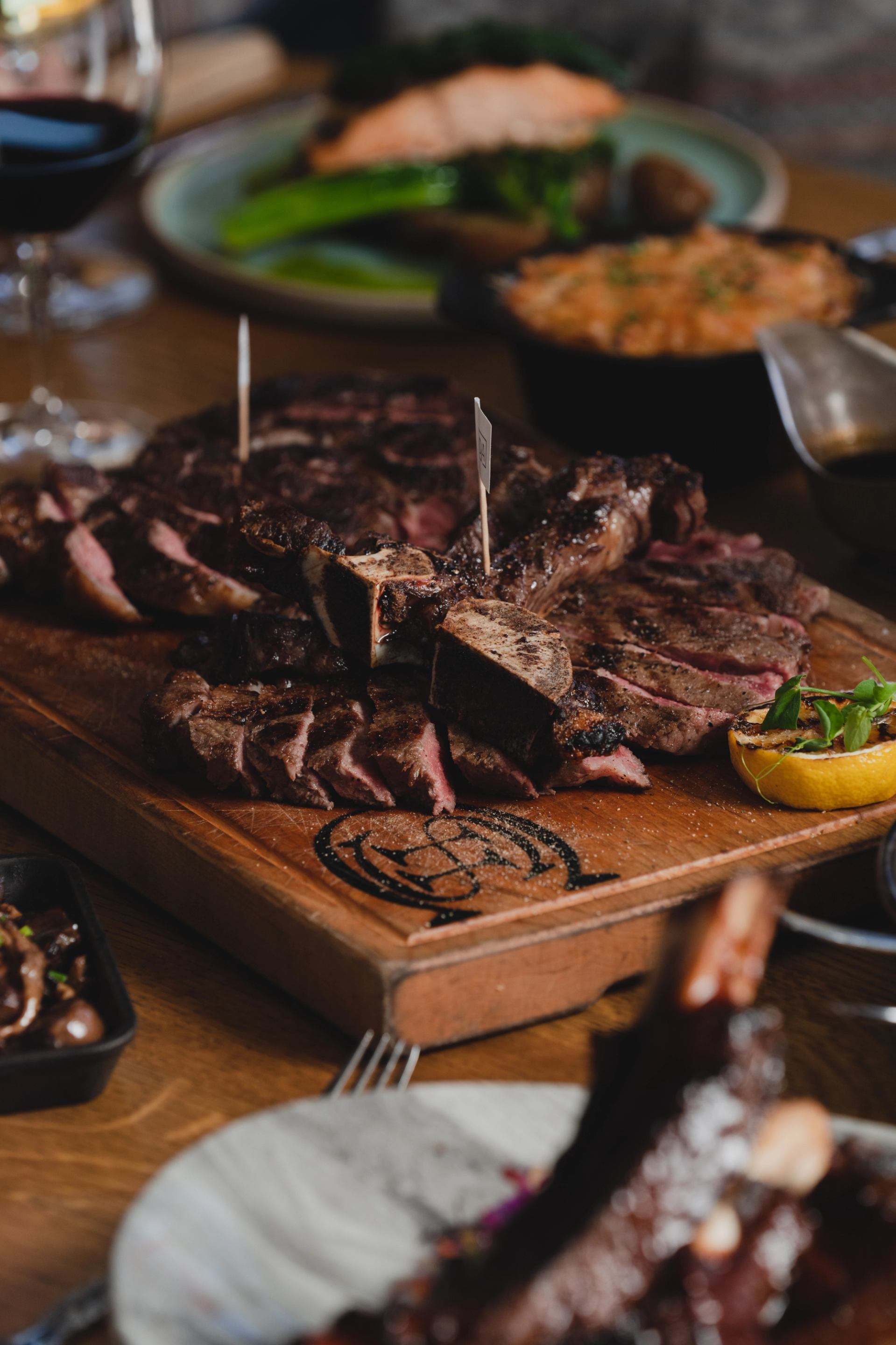 Close-up of a large, sliced grilled steak on a wooden board at a restaurant table.