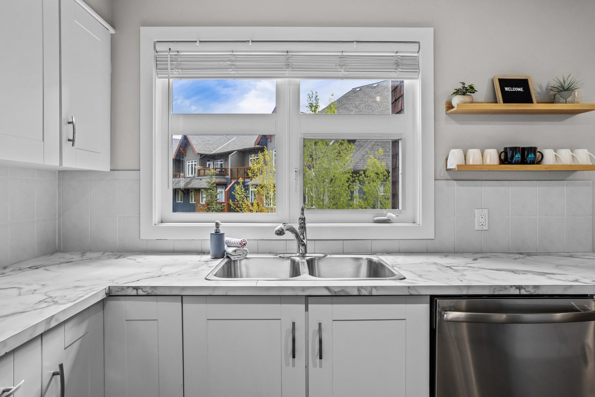 White kitchen with marble-patterned counters, double sink, window and open shelves.