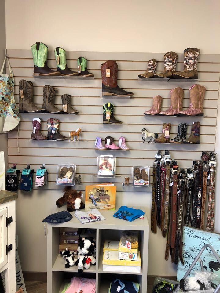 Wall display of cowboy boots, belts, keychains, and hats in a retail store.