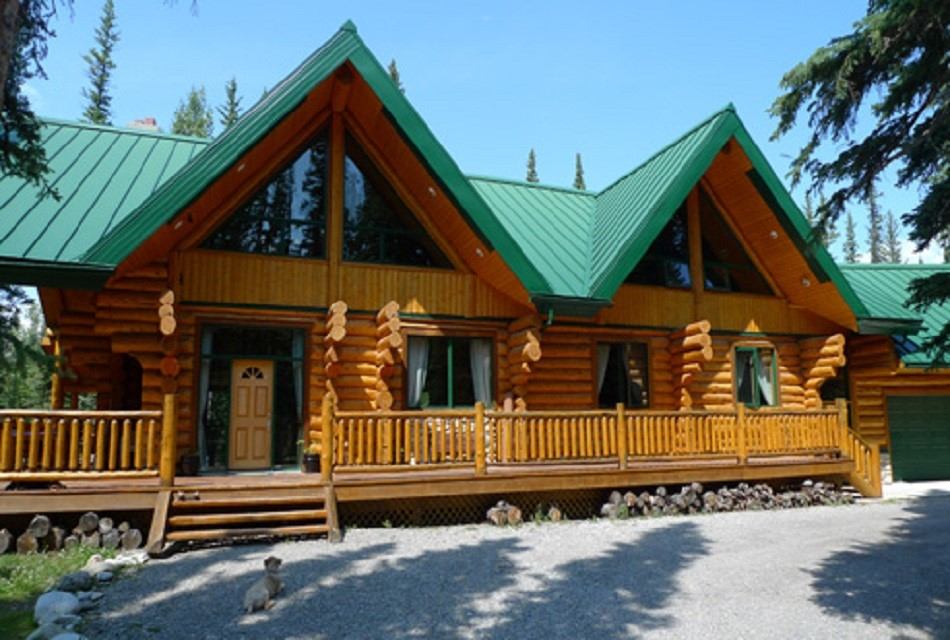 Riverside Chateau log cabin with green roof, porch, and forest backdrop.