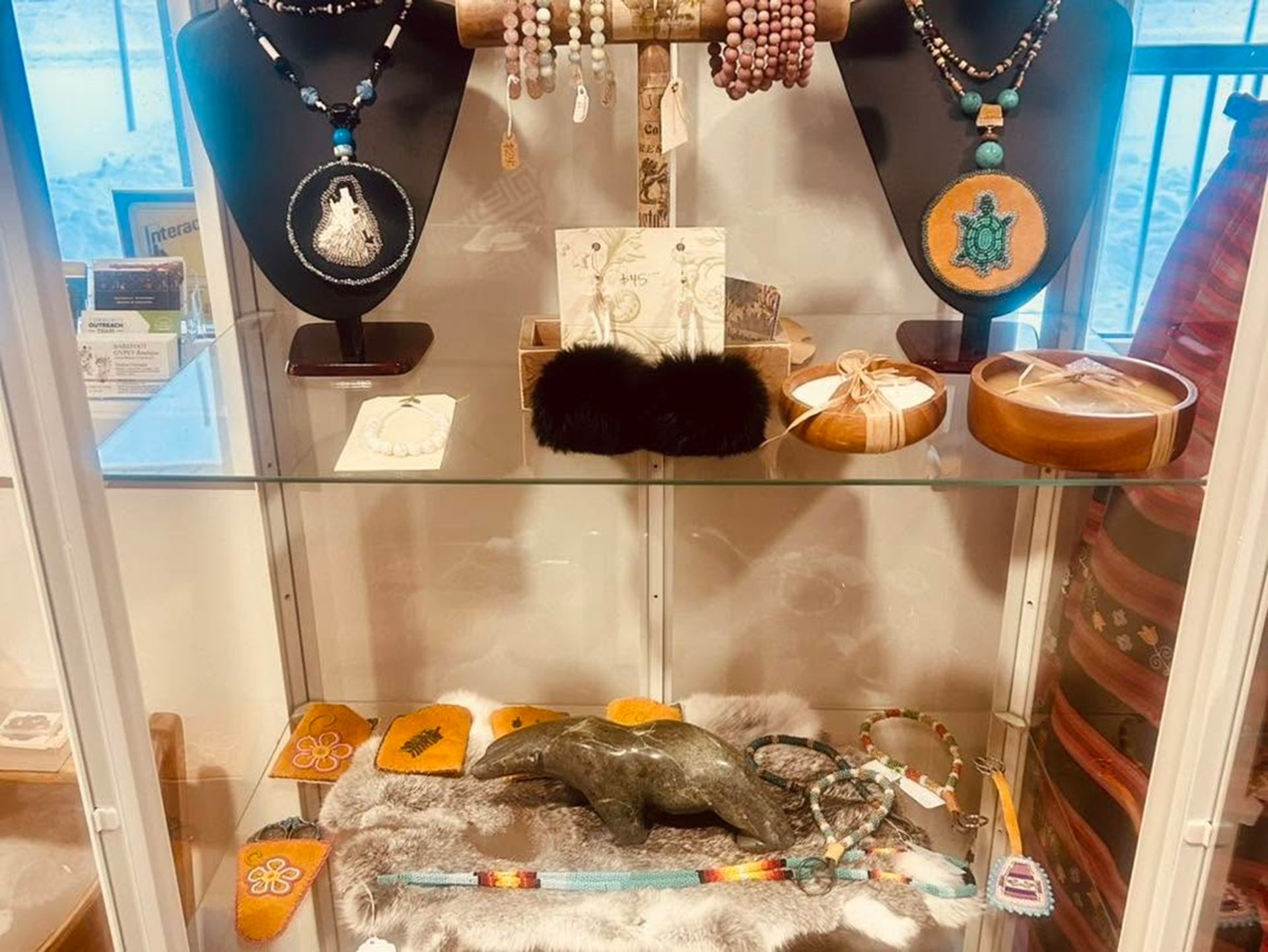 Display case with beaded necklaces, bracelets, fur accessories and carved stone animal.