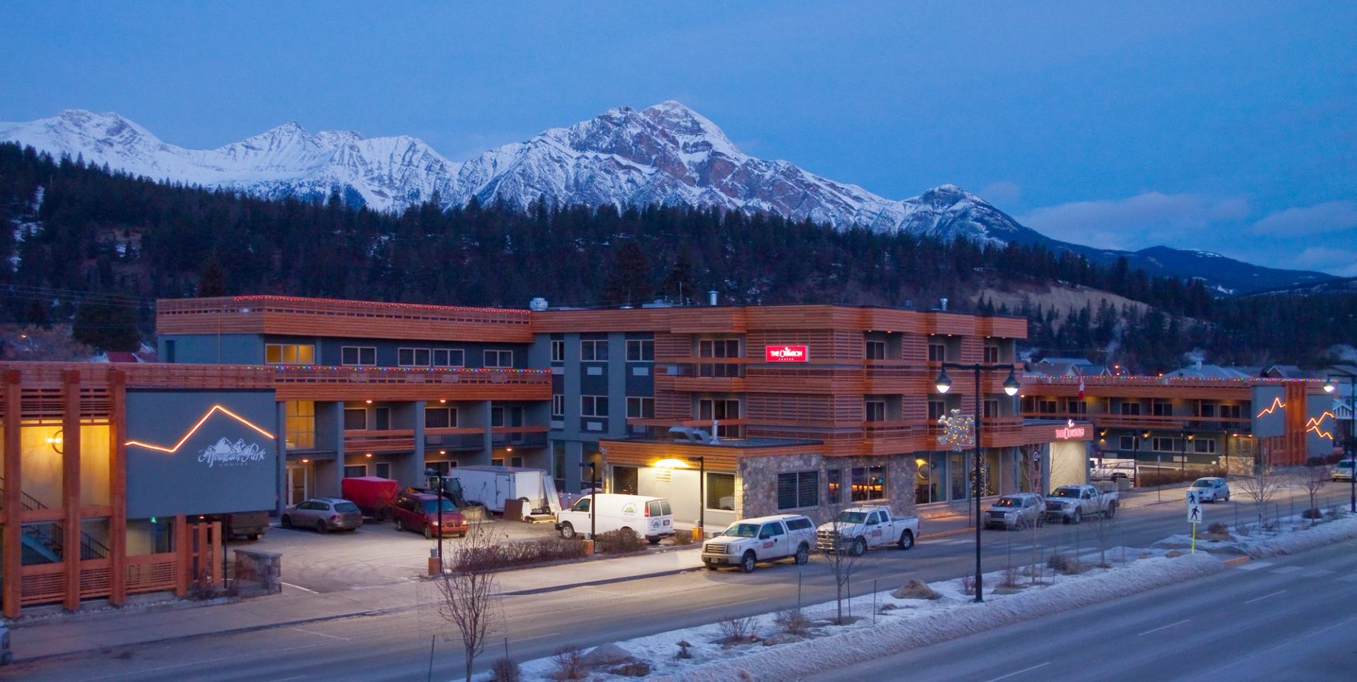 Mountain lodge at dusk with snowy peaks in the background.
