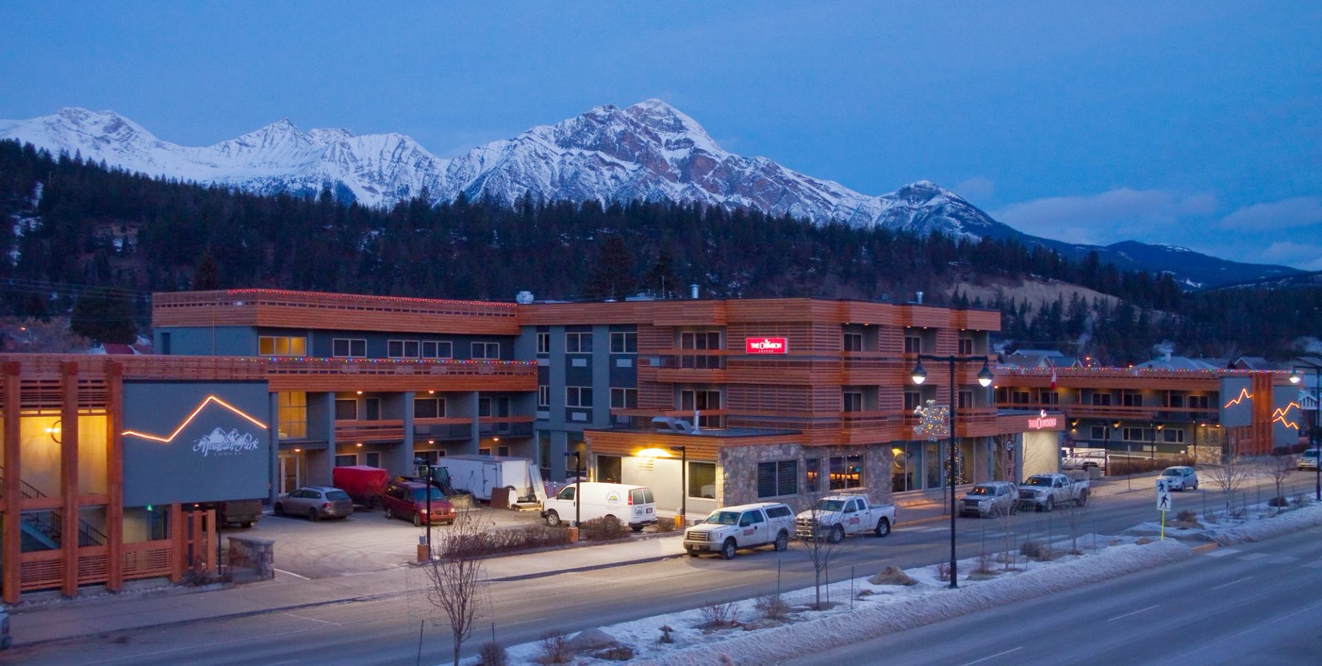 Mountain lodge at dusk with snowy peaks in the background.