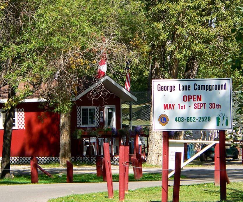 Entrance of George Lane Campground with red building, trees, and sign showing open dates.