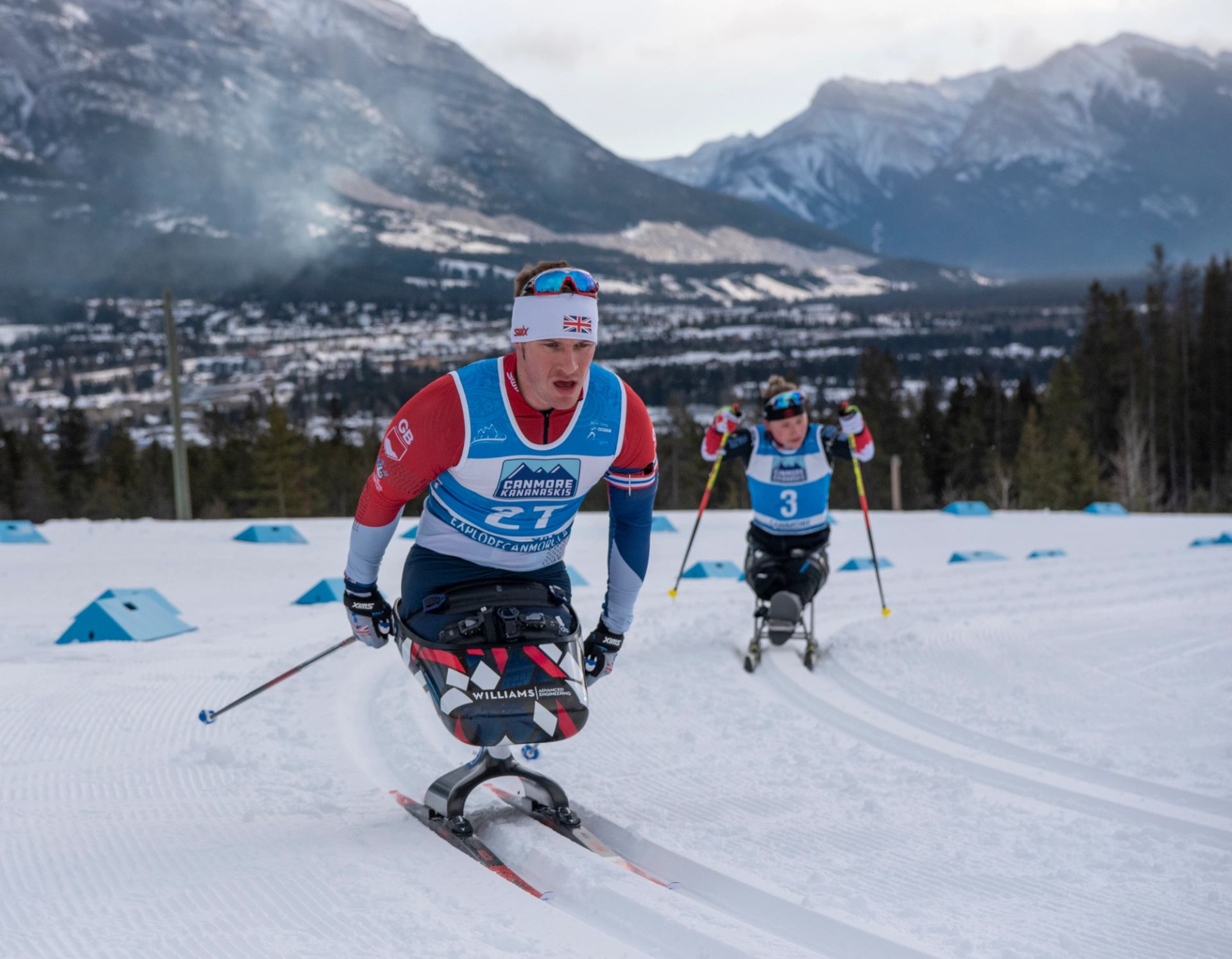 Sit-ski athletes racing on a snowy track in the mountains.